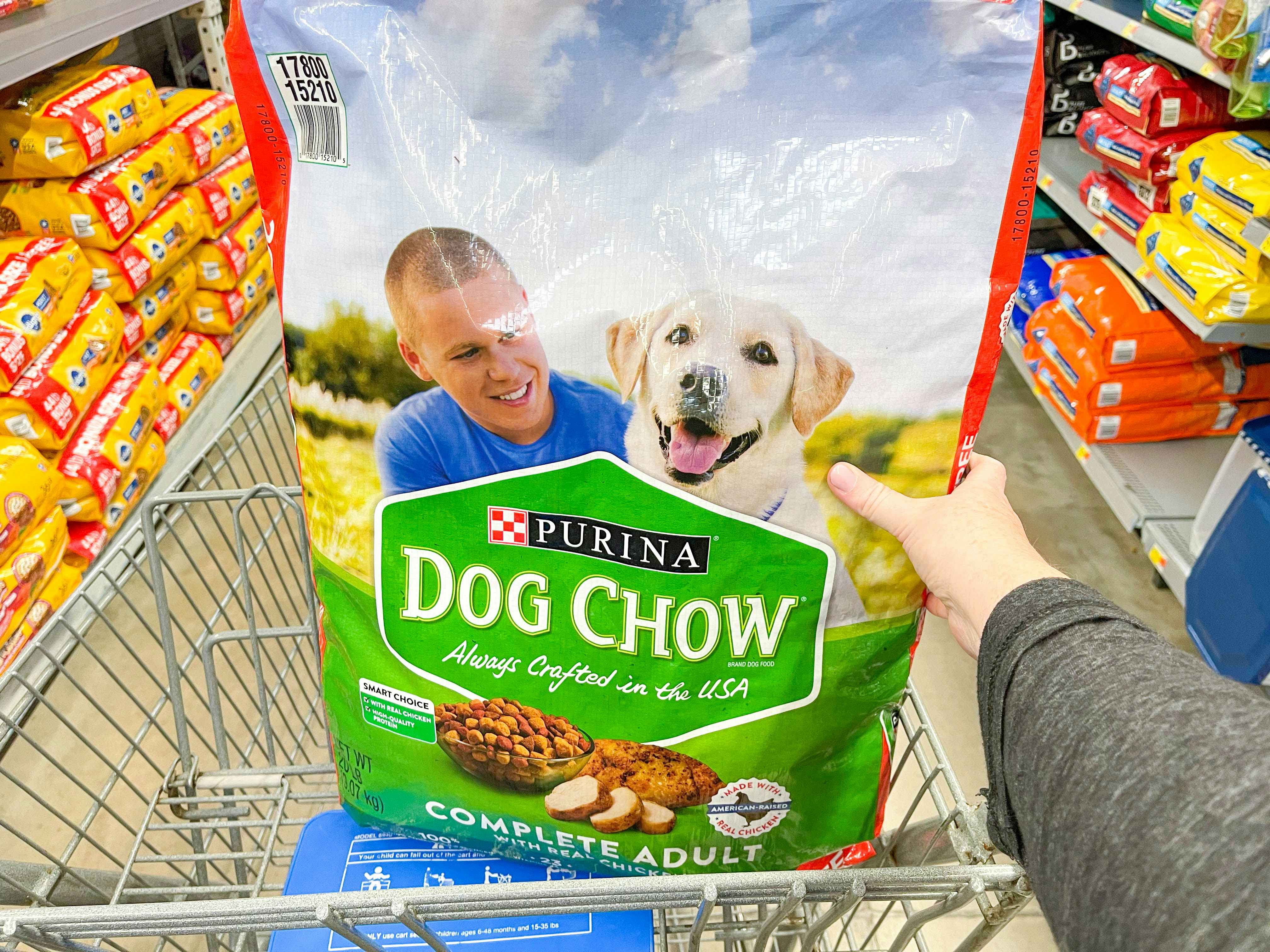 a walmart cart with a large bag of dog food in the top basket being held by a person 