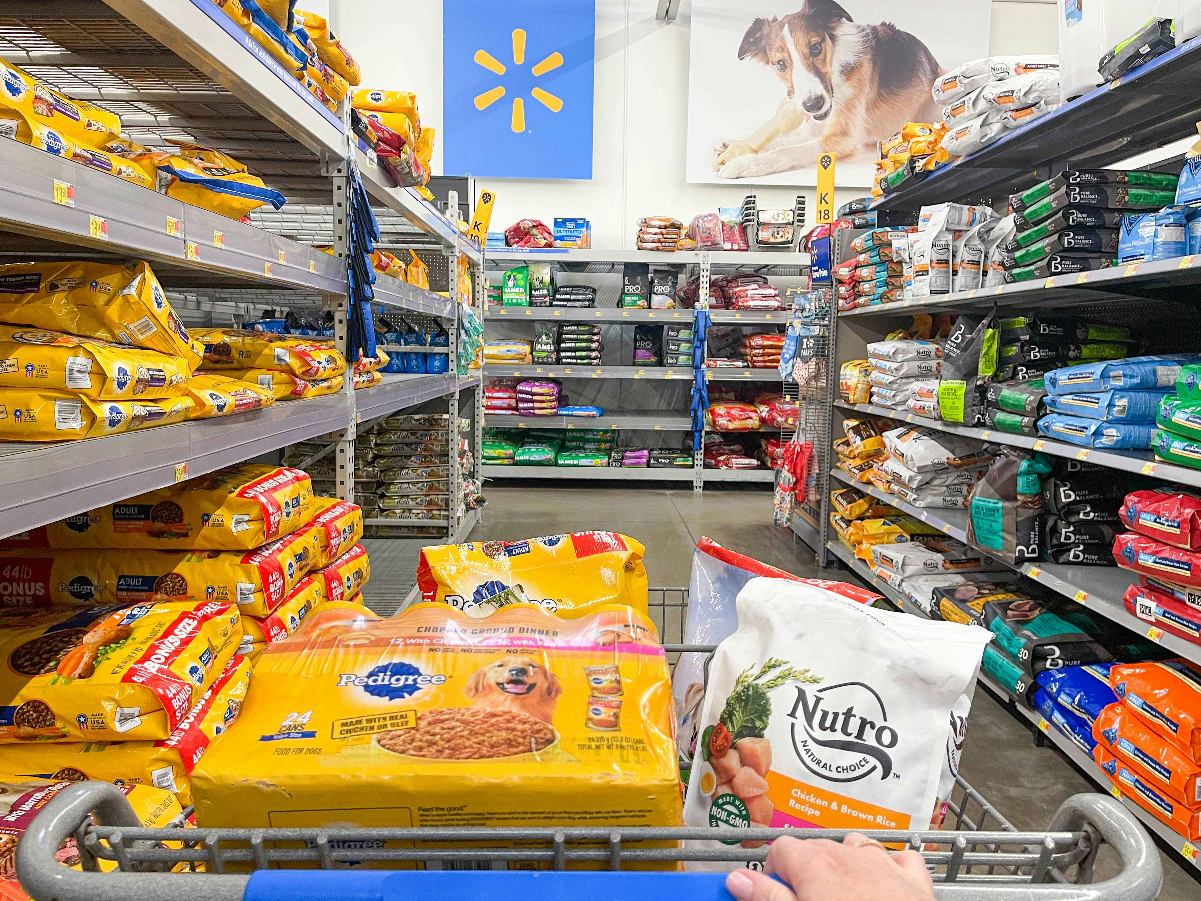 a person pushing a cart filled with dog food in walmart pet section 