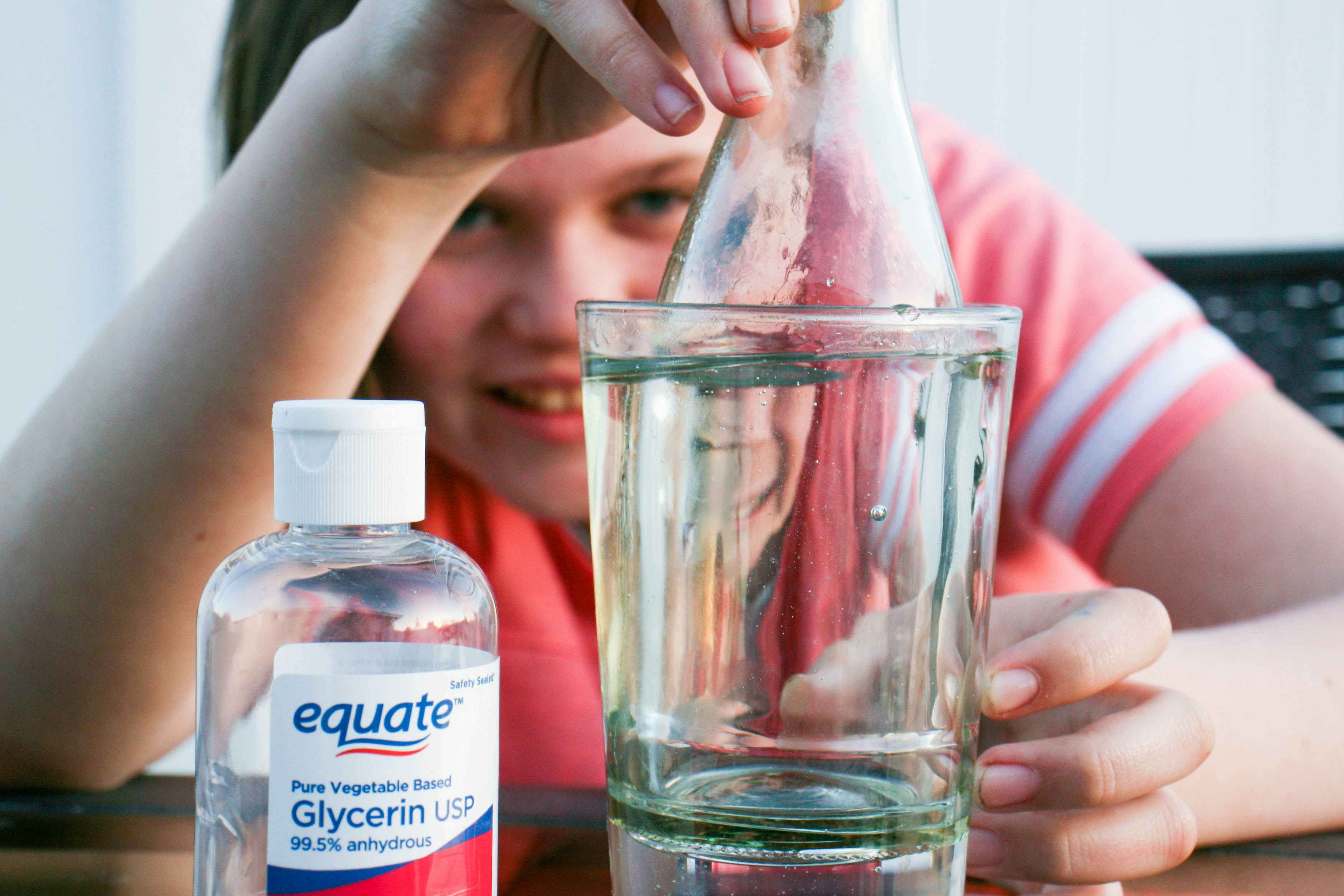 a child pouring glycerin into a cup with a glass bottle inside 