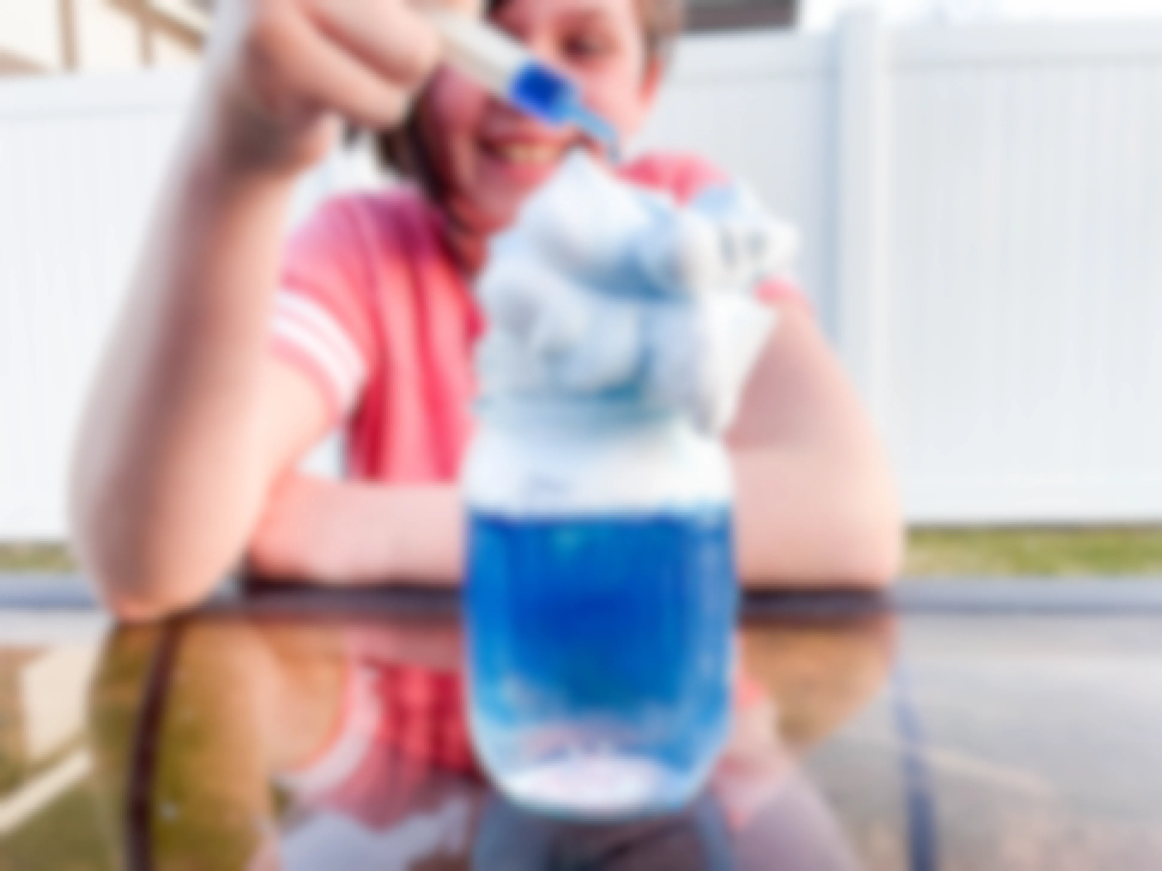 a kid with a syringe with blue dye dropping liquid into a mason jar with water and shaving cream
