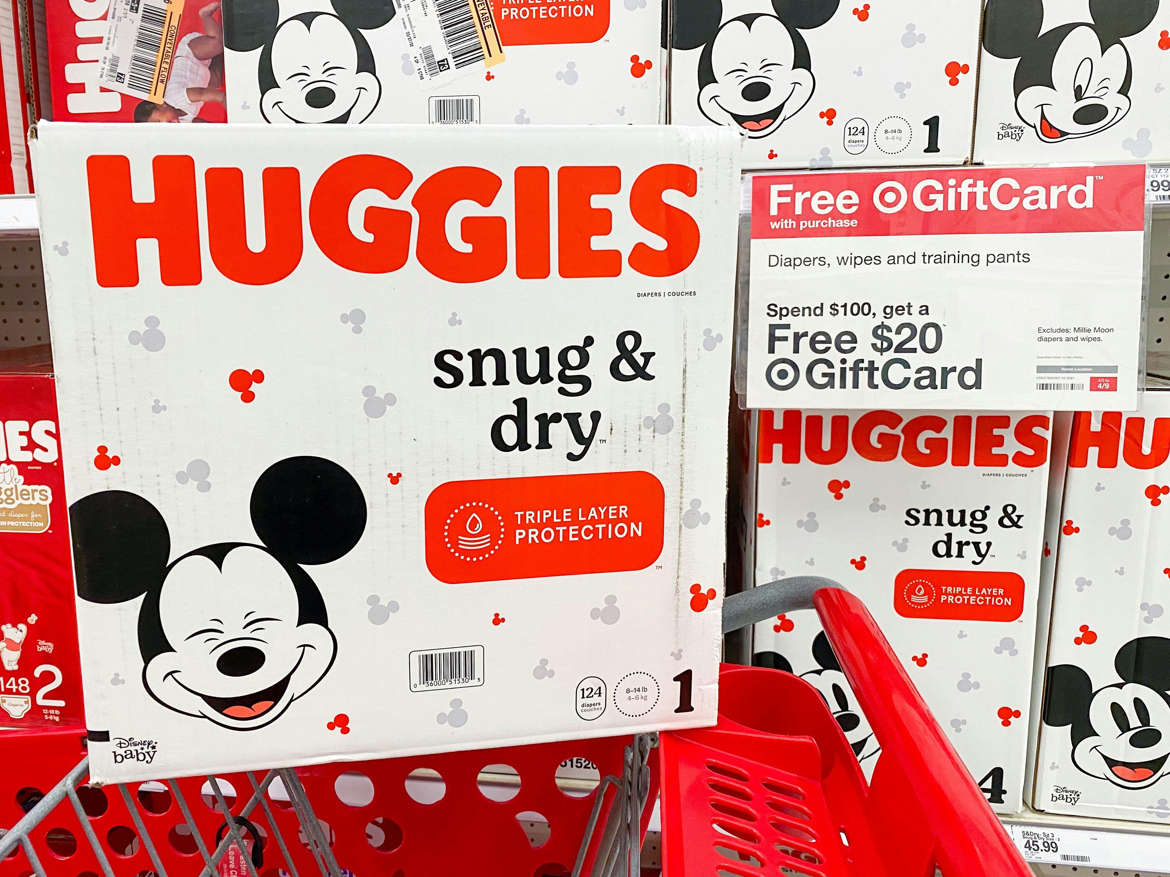 A box of Huggies Snug & Dry diapers sitting on a Target shopping cart in front of a sign advertising a Free $20 Target gift card when you spend $100 or more on diapers, wipes, and training pants.