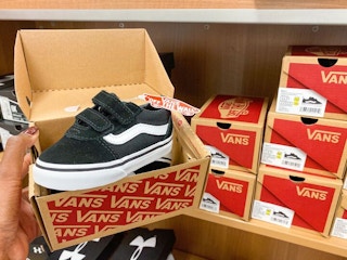 A person holding a pair of kids van's shoes next to shoe boxes in a store.