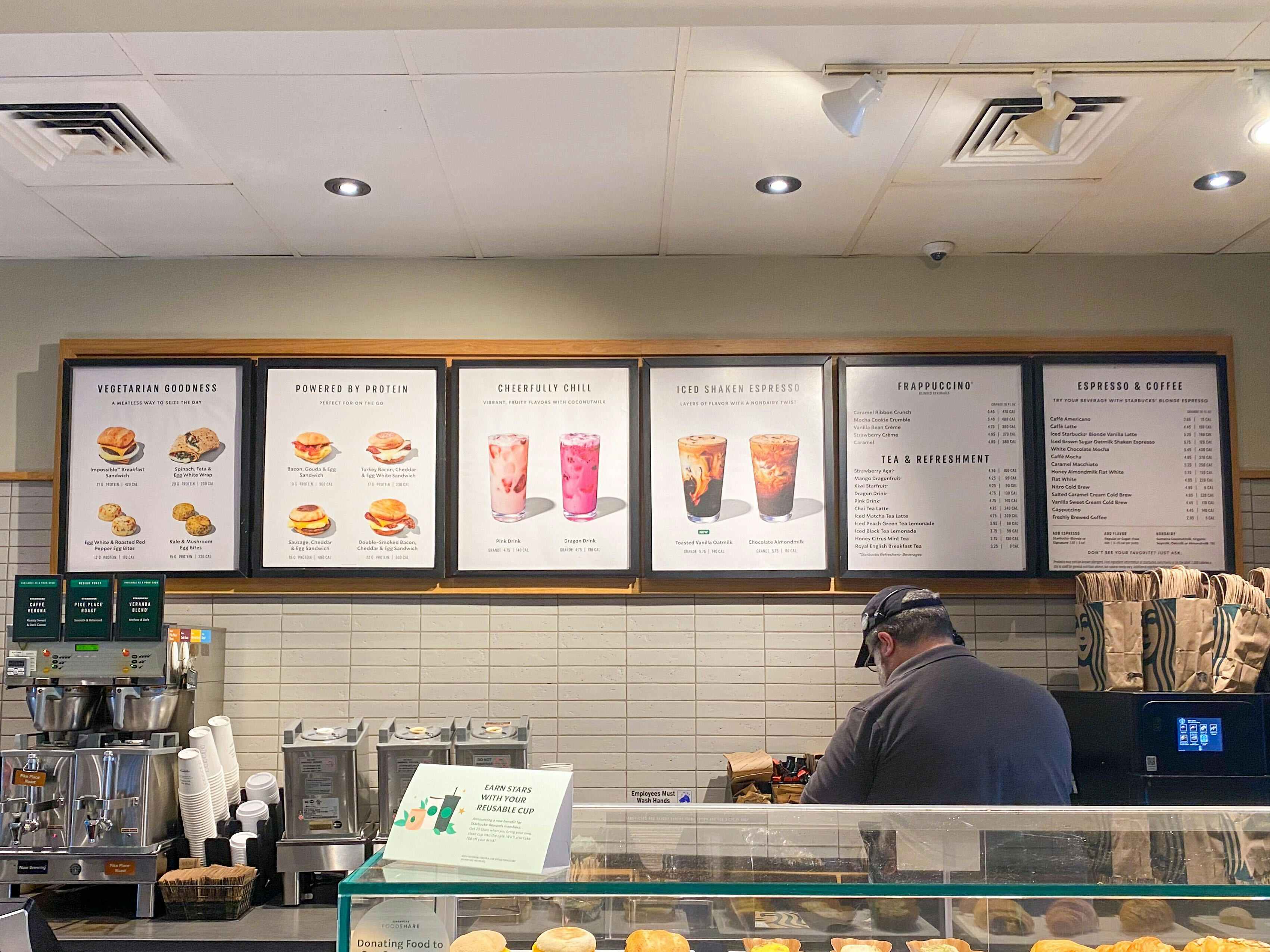 The Starbucks menu on the wall behind the counter, above a Starbucks employee who is working.