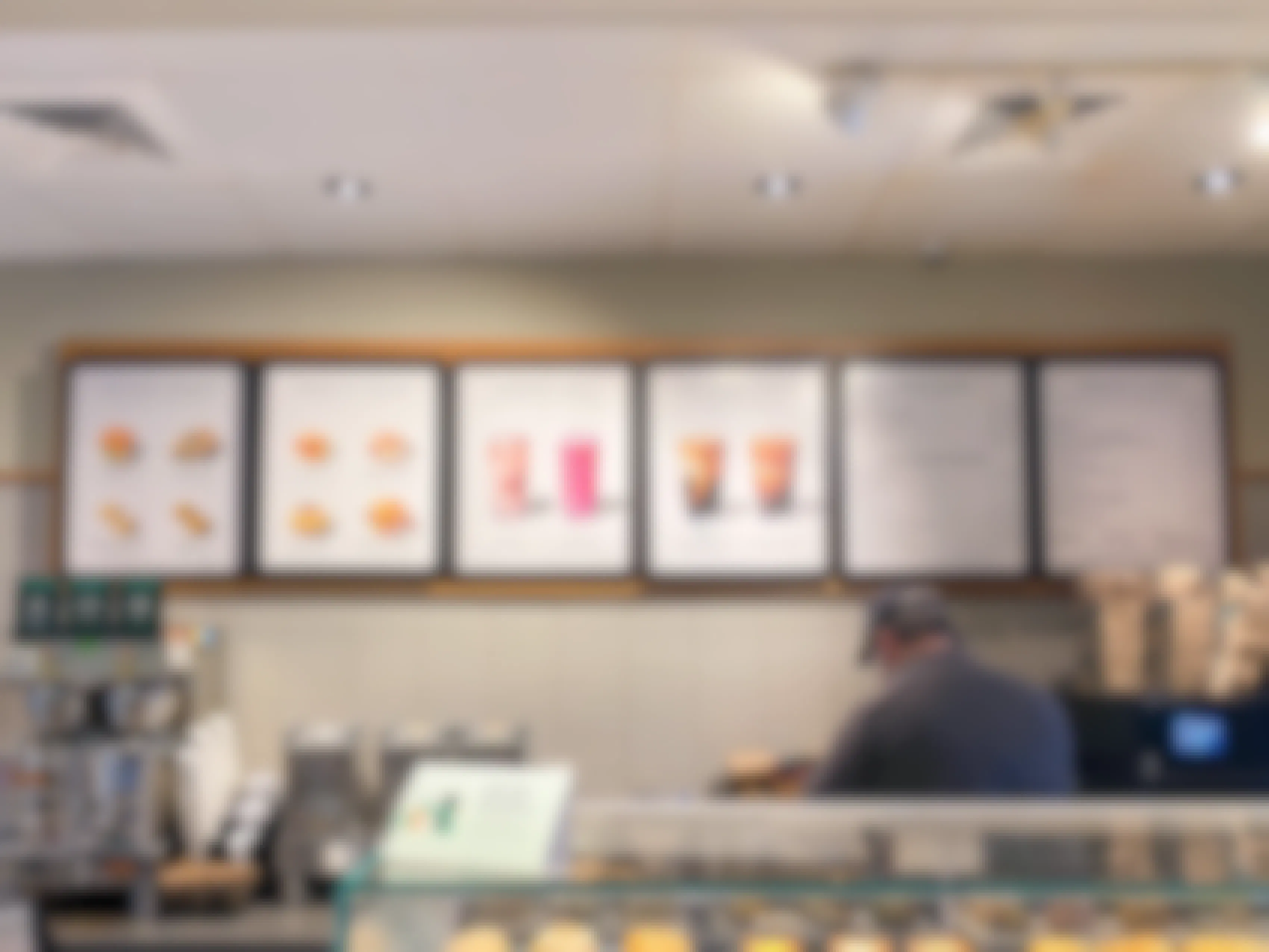 The Starbucks menu on the wall behind the counter, above a Starbucks employee who is working.