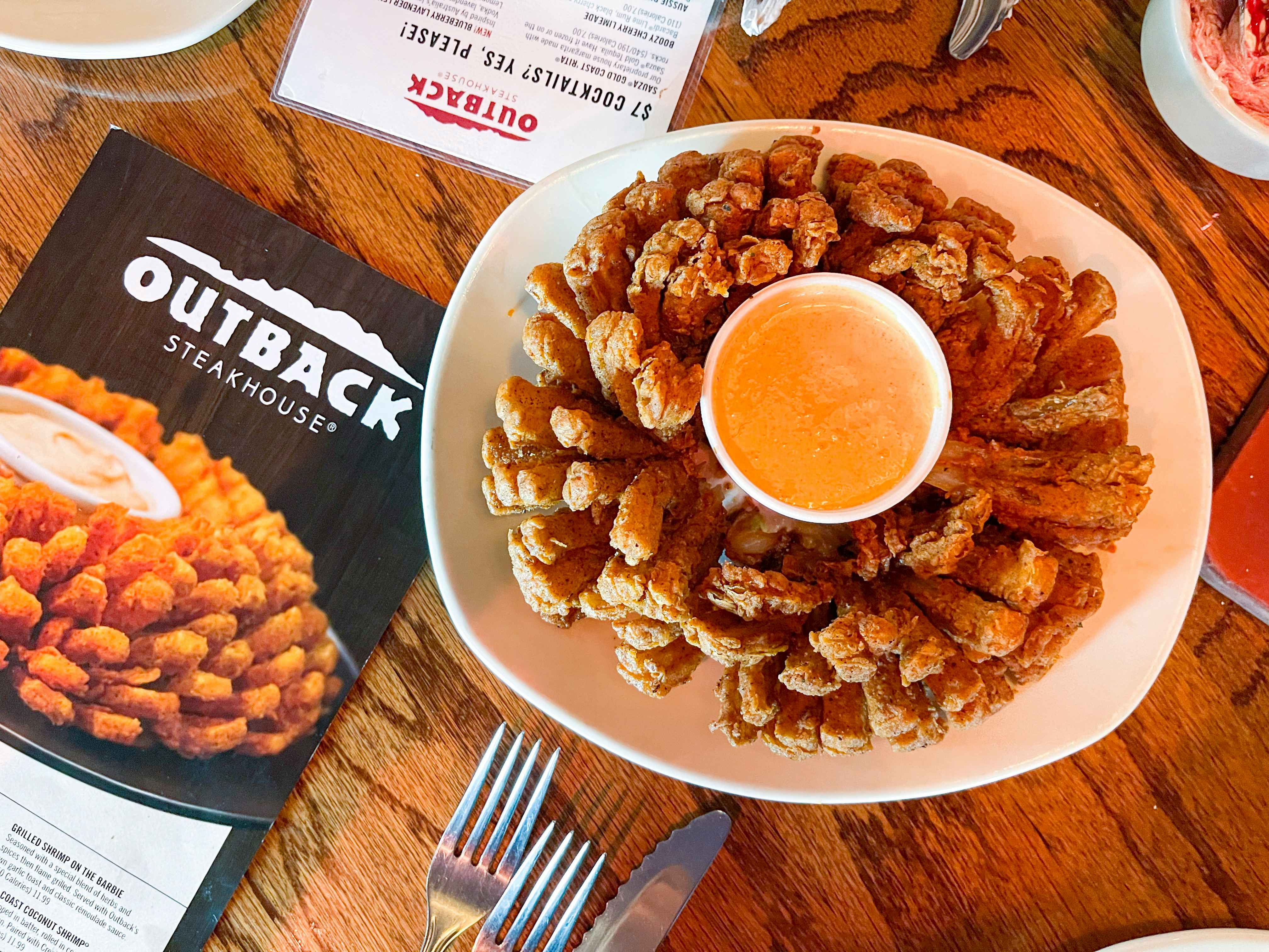 A Blooming Onion served on a table next to an Outback Steakhouse menu