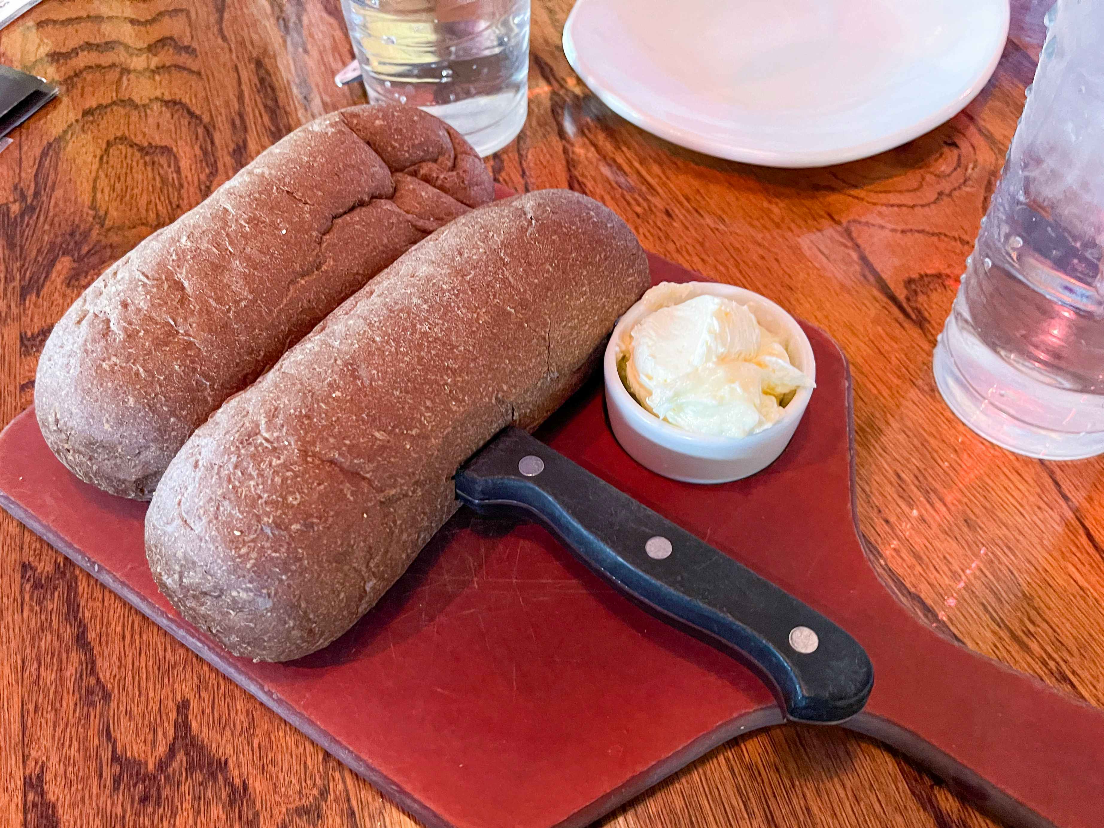 Some bread served on a platter with a knife and a cup of butter at Outback Steakhouse.