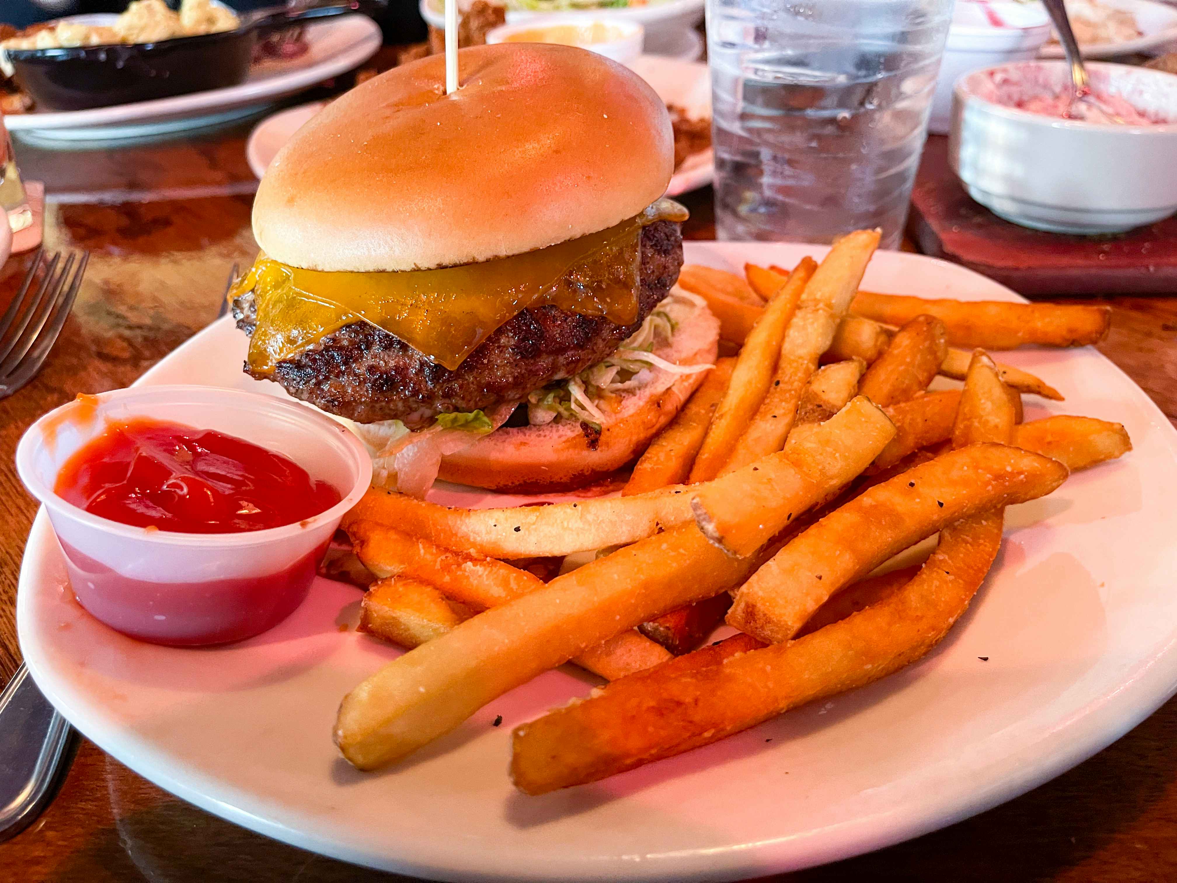An Outback Burger and fries on a plate with a cup of ketchup at Outback Steakhouse.