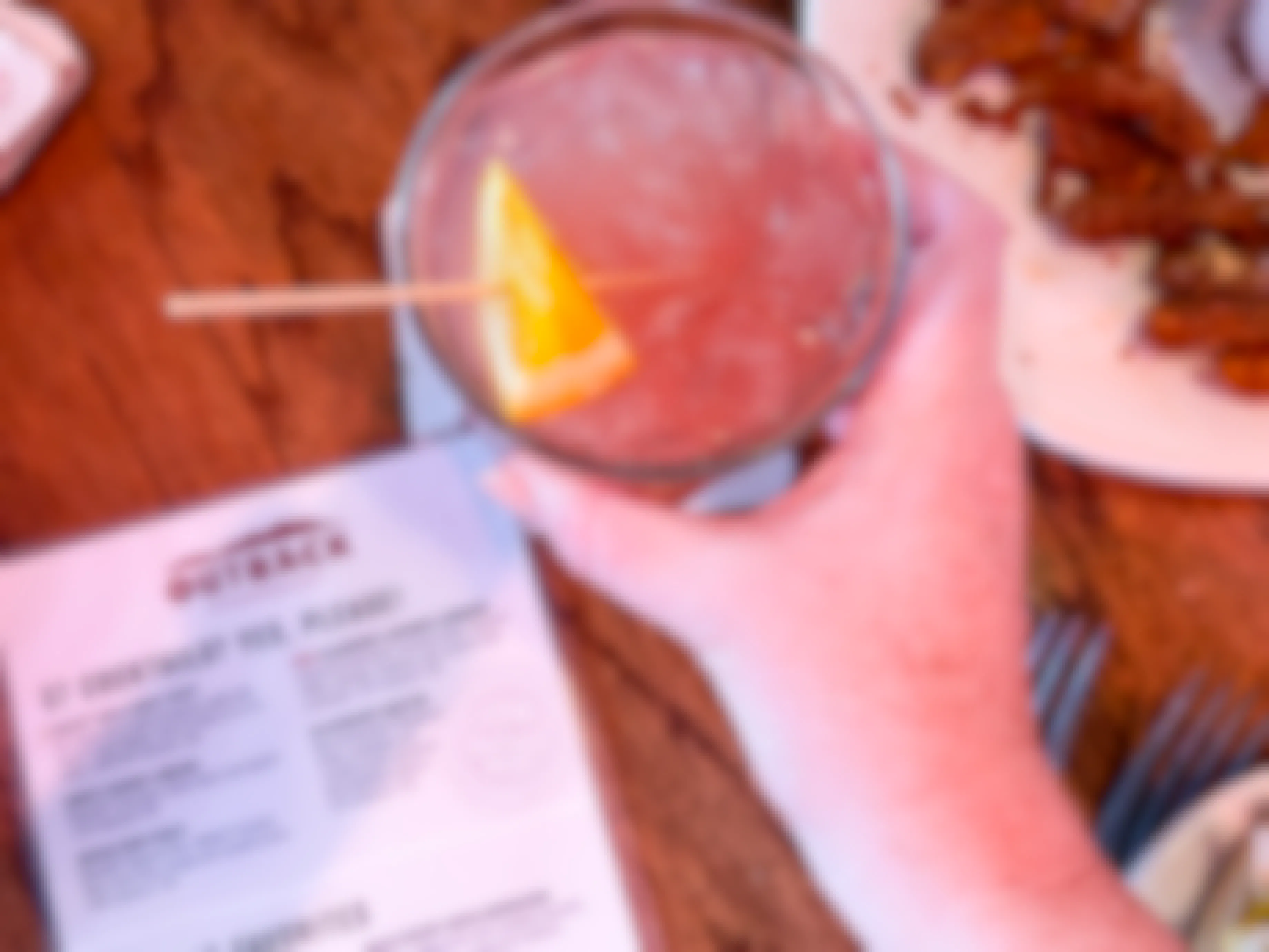 A person's hand grabbing a cocktail drink sitting on a table next to an Outback Steakhouse drink menu.