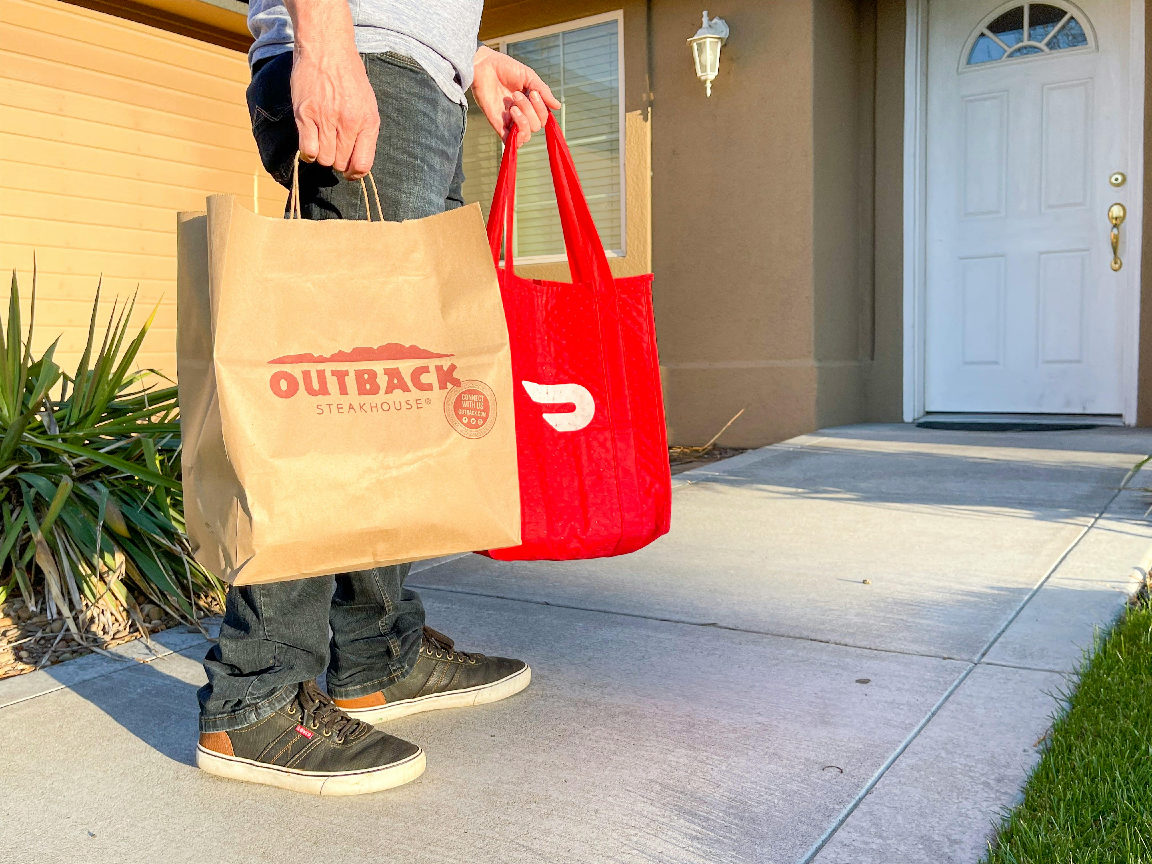 a DoorDash driver holding multiple delivery bags and walking up to the front door of a house