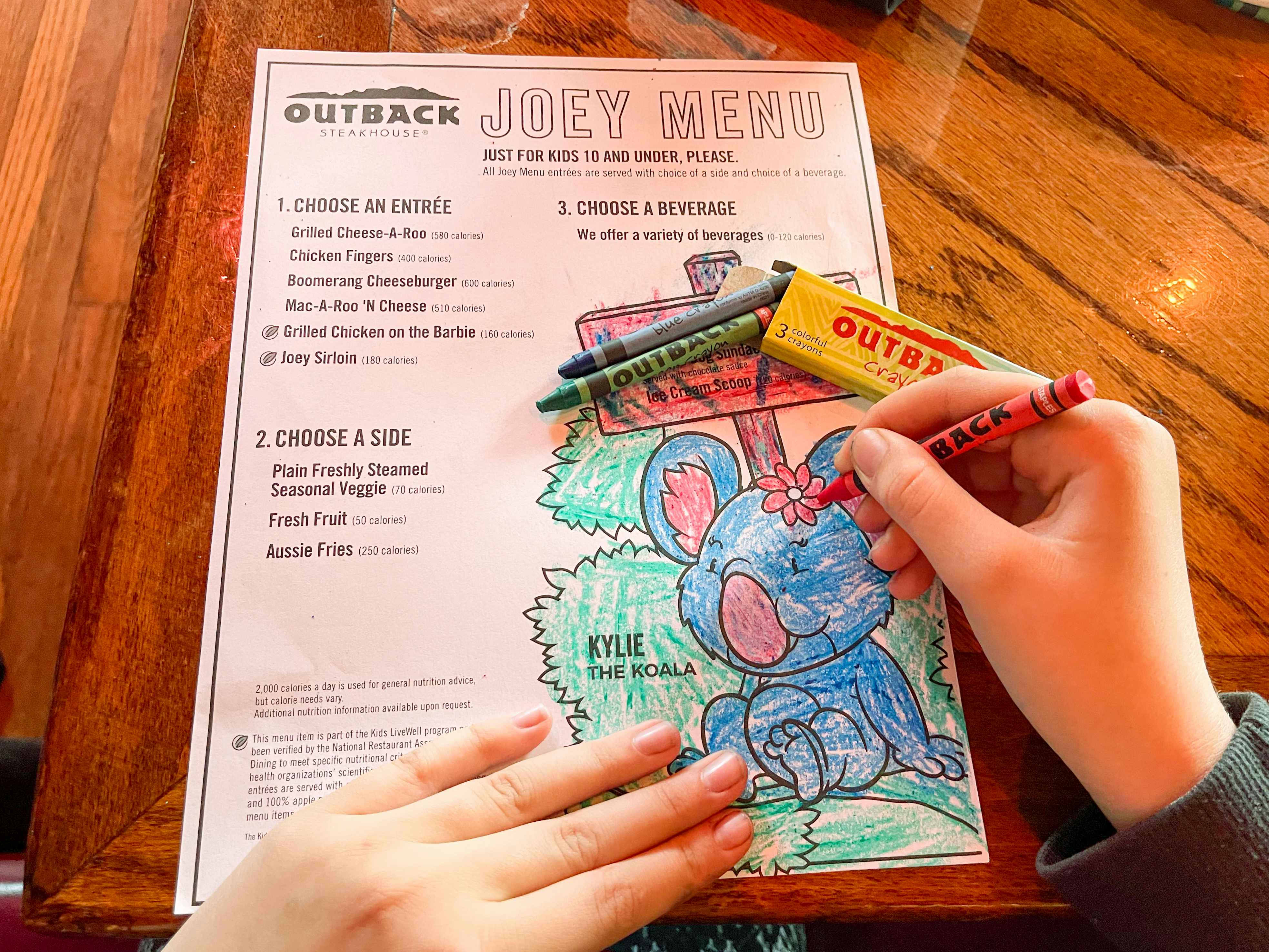 A person coloring the Outback Steakhouse Joey Menu with crayons.