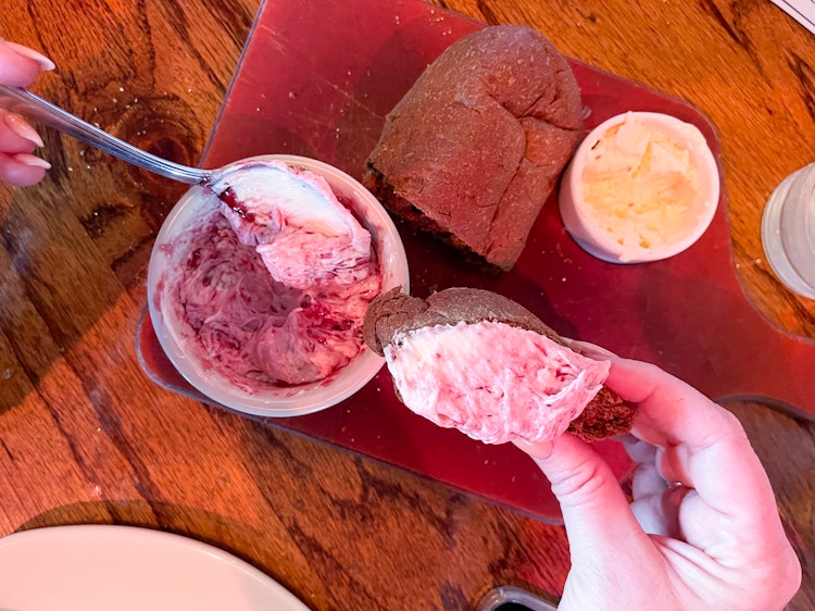 A person using a spoon to mix raspberry sauce with a cup of butter to spread on their bread at Outback Steakhouse.