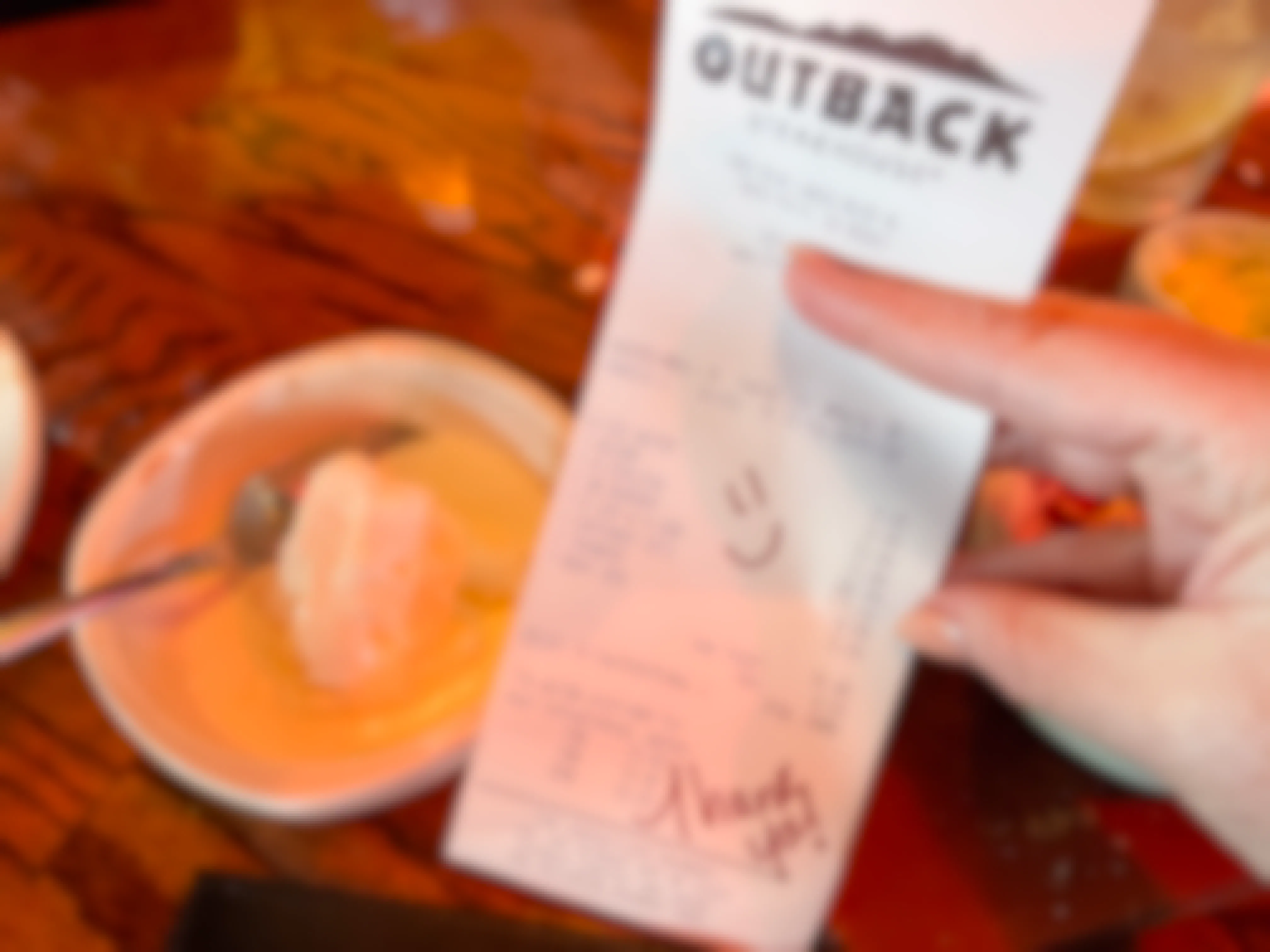 A person's hand holding up an Outback Steakhouse receipt with a free birthday item listed next to a bowl of partially eaten ice cream.