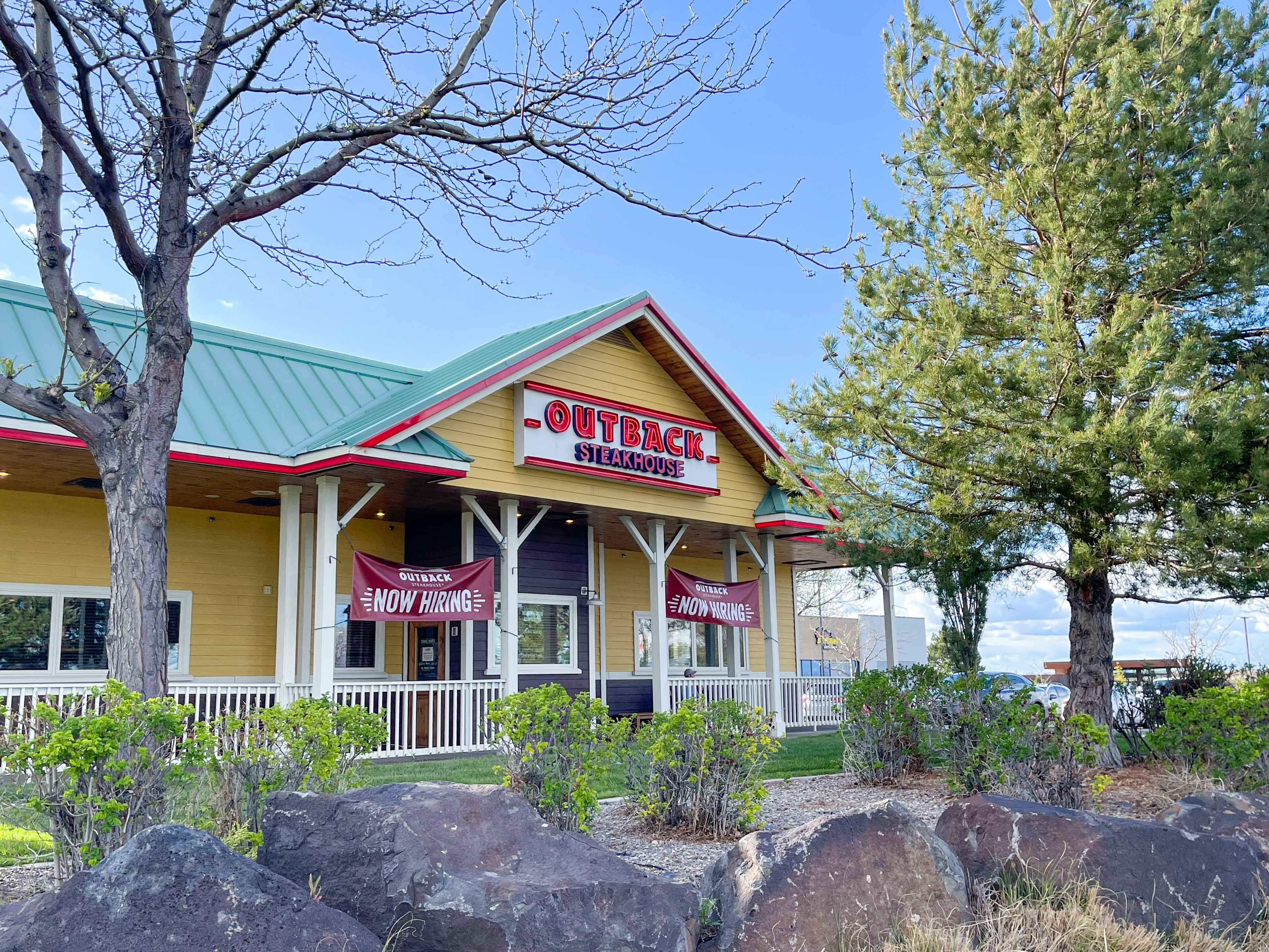 An Outback Steakhouse storefront with trees and rocks in the foreground.