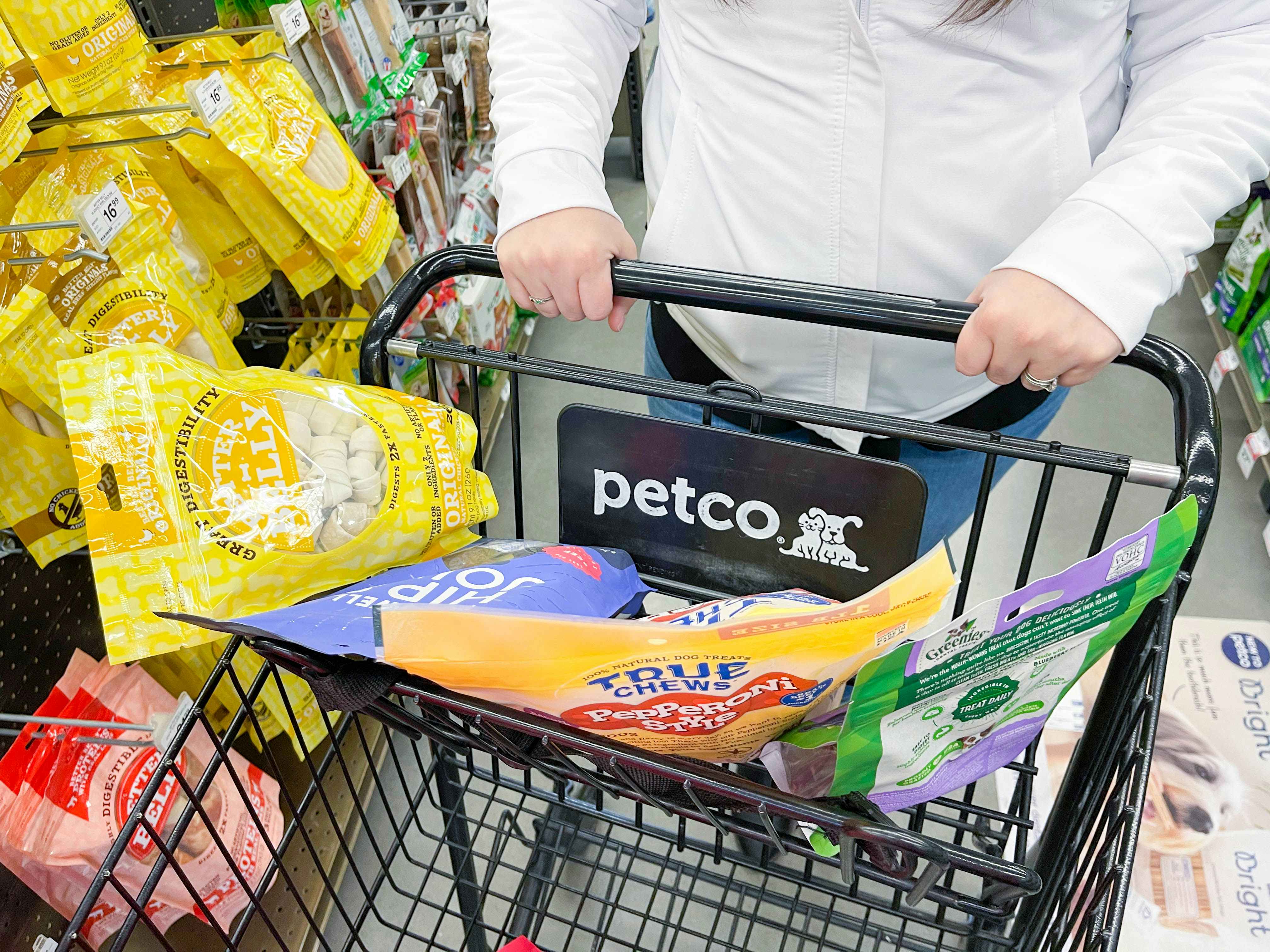 a person pushing a petco shopping cart with dog treats in top part of cart