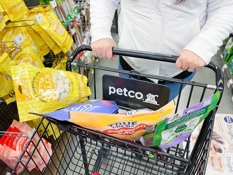 a person pushing a petco shopping cart with dog treats in top part of cart