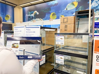 a person holding an aquarium in store around other tanks stacked up