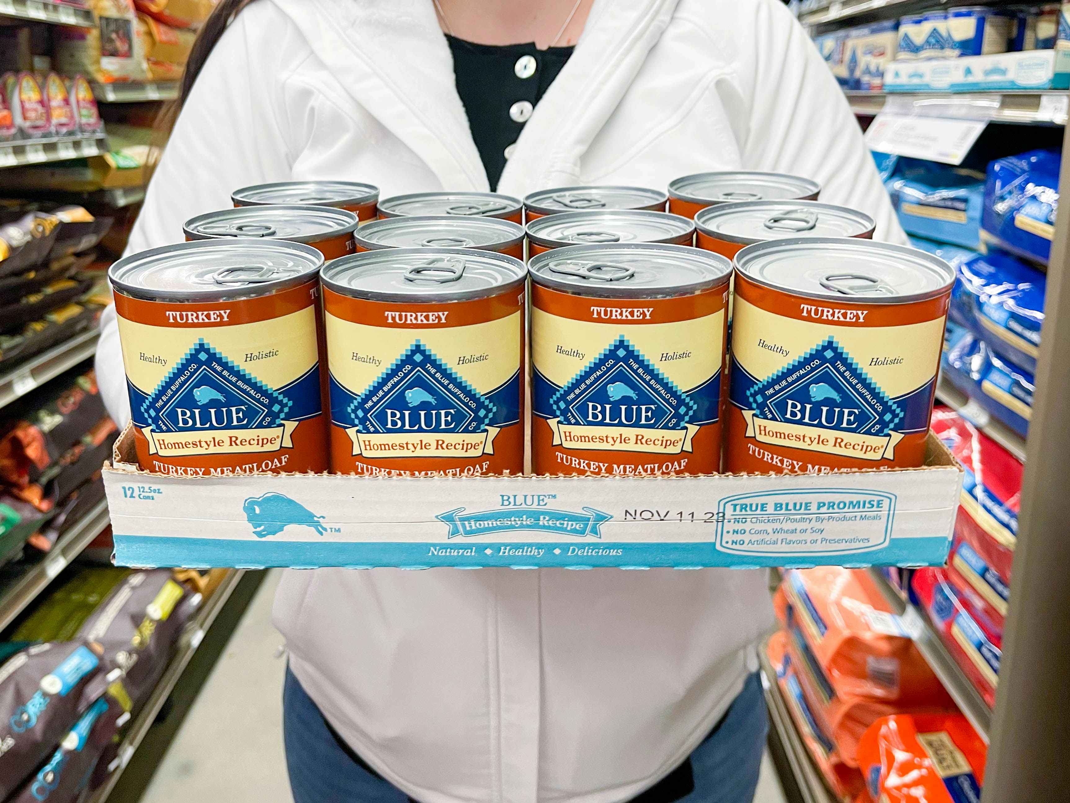 a person holding a tray of 12 blue turkey meatloaf wet dog food cans in store