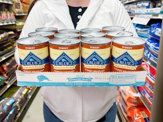 a person holding a tray of 12 blue turkey meatloaf wet dog food cans in store