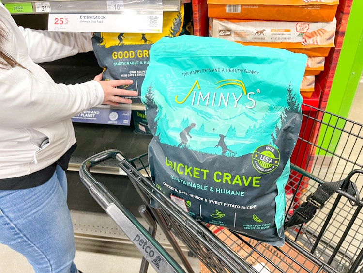 a person grabbing dog food off shelf with a bag of dog food in cart