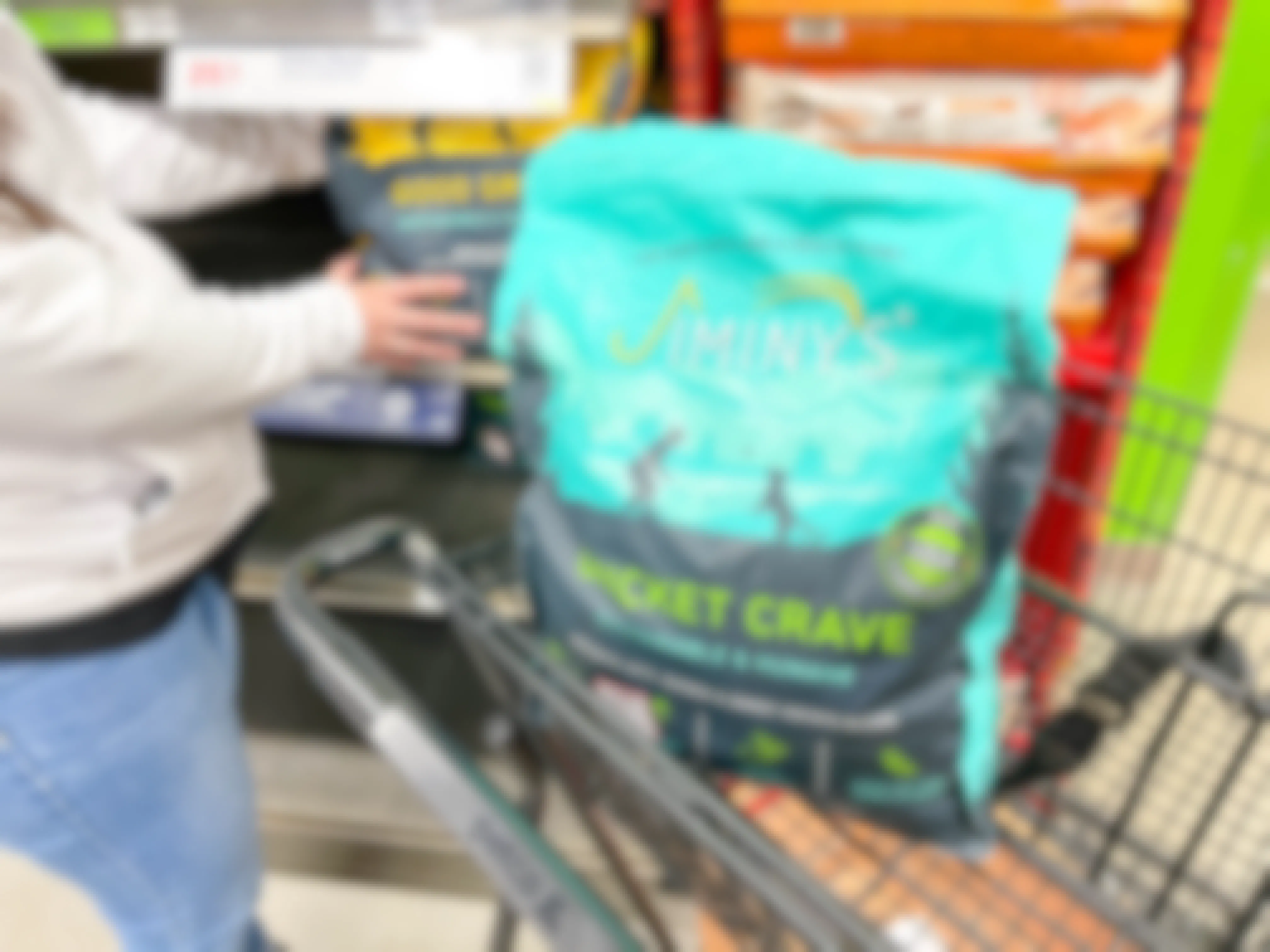 a person grabbing dog food off shelf with a bag of dog food in cart