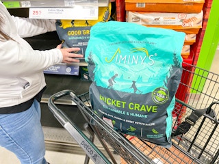 a person grabbing dog food off shelf with a bag of dog food in cart