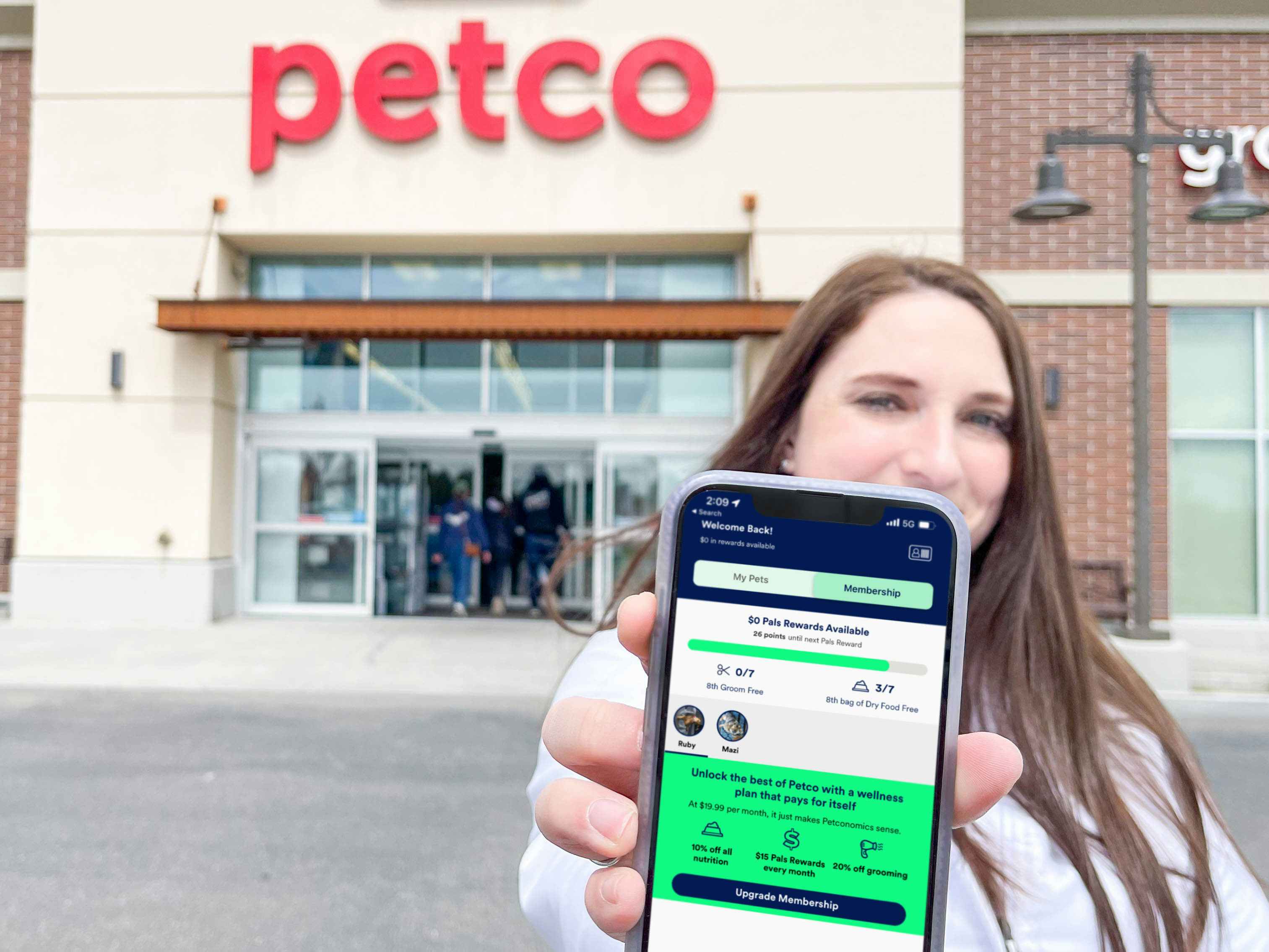 a woman holding a cellphone with pals rewards on screen standing in front of a petco 
