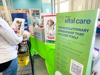 a person pushing a shopping cart in petco store near large vital care sign 