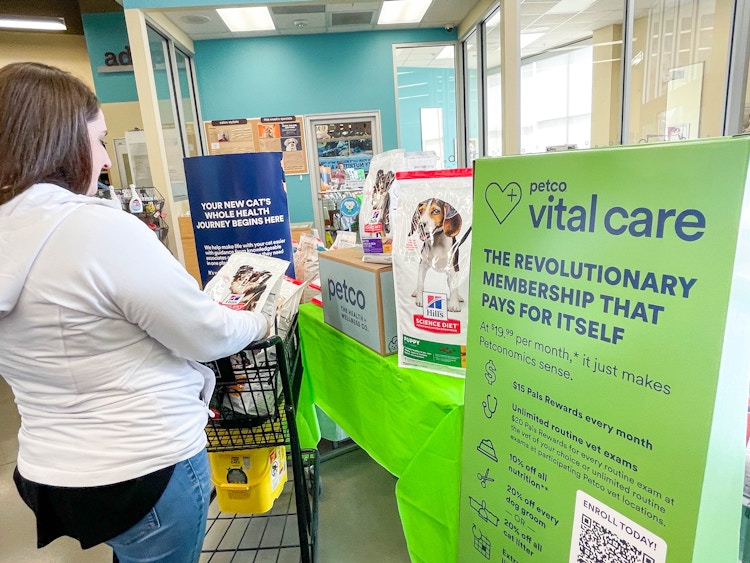 a person pushing a shopping cart in petco store near large vital care sign