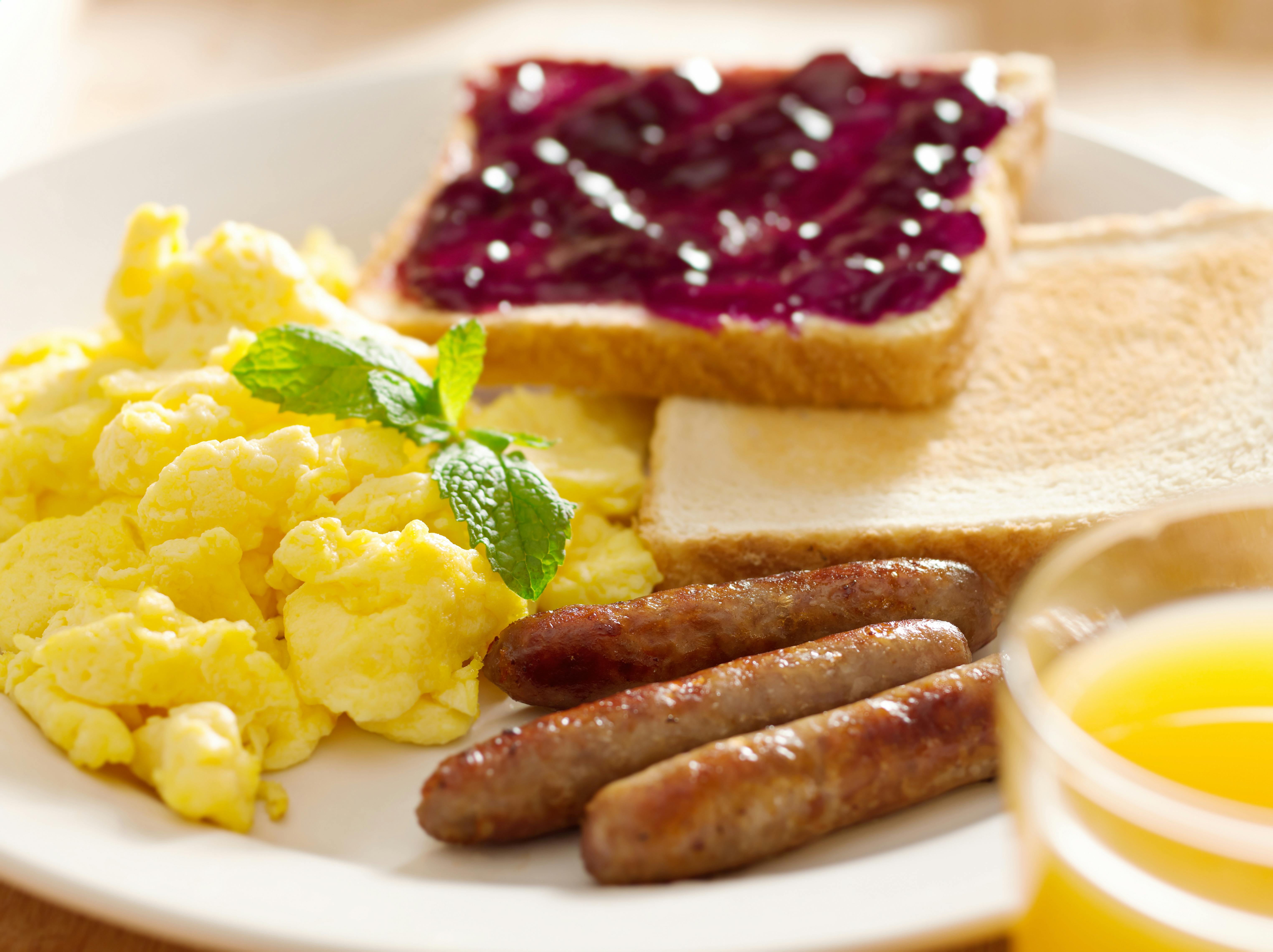 scrambled eggs, toast with jam, and sausage on a plate with a glass of orange juice