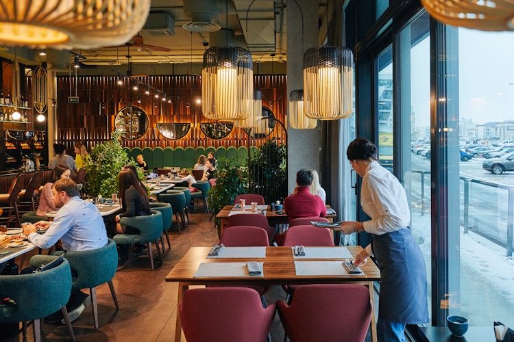 The indoor seating area of a beautiful restaurant with a waitress setting silverware on a table