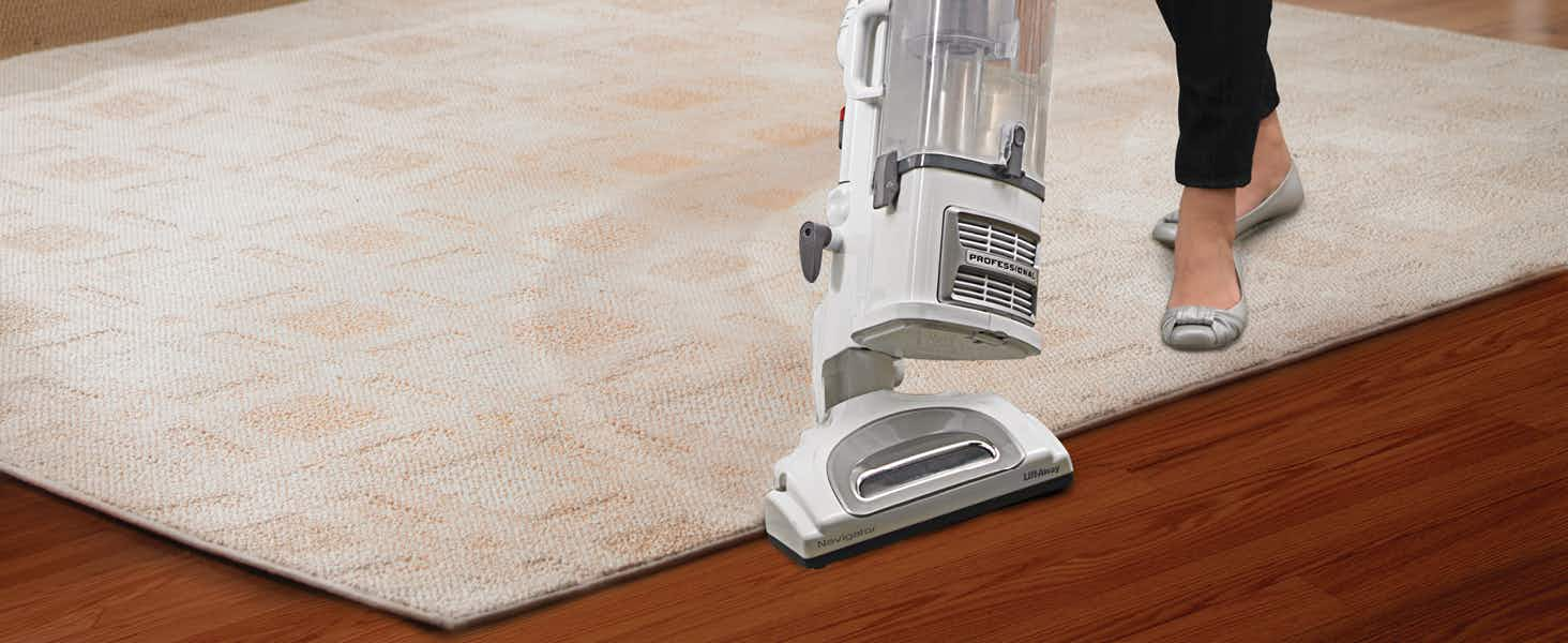 A person pushing a Shark vacuum across a rug on a hardwood floor.