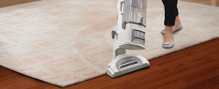 A person pushing a Shark vacuum across a rug on a hardwood floor.