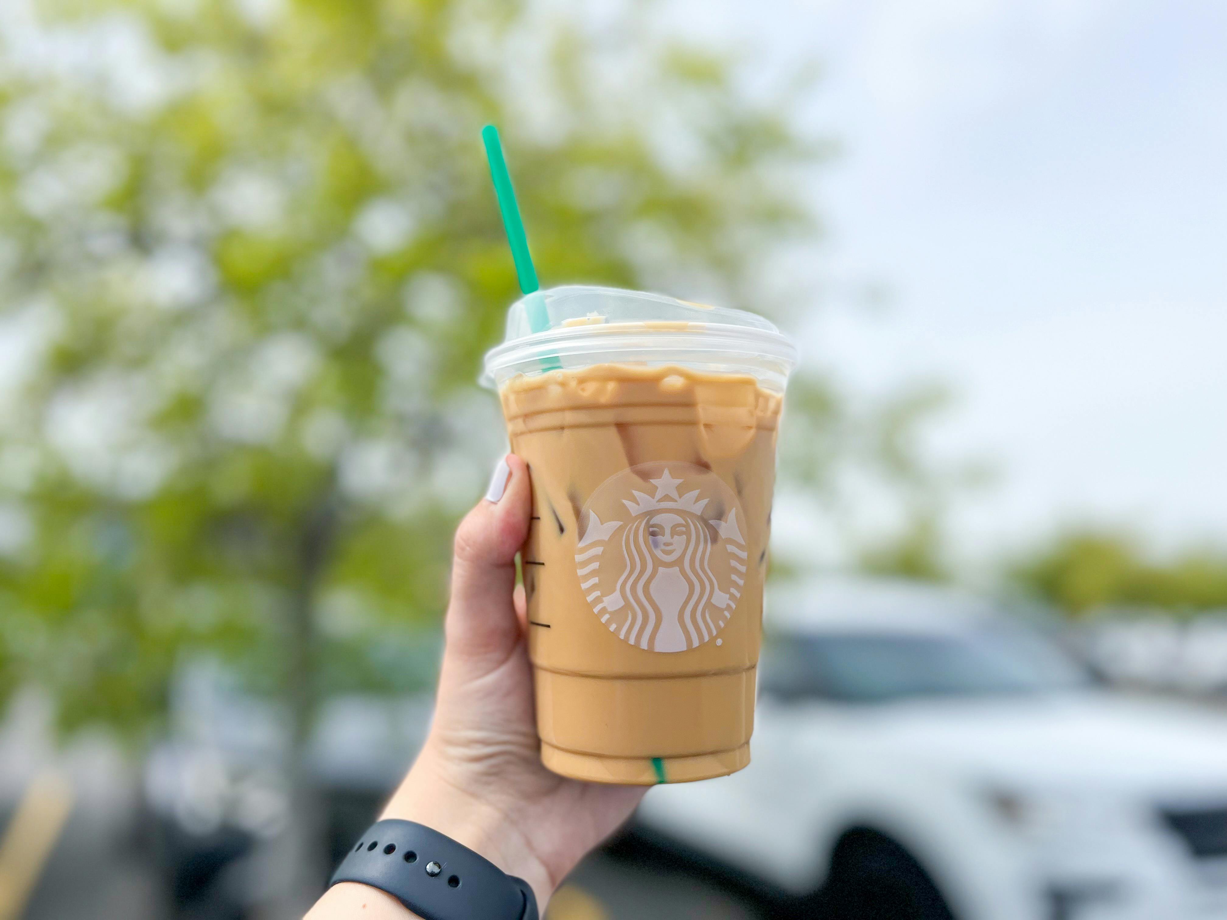 A person's hand holding up an iced Starbucks coffee while outside.