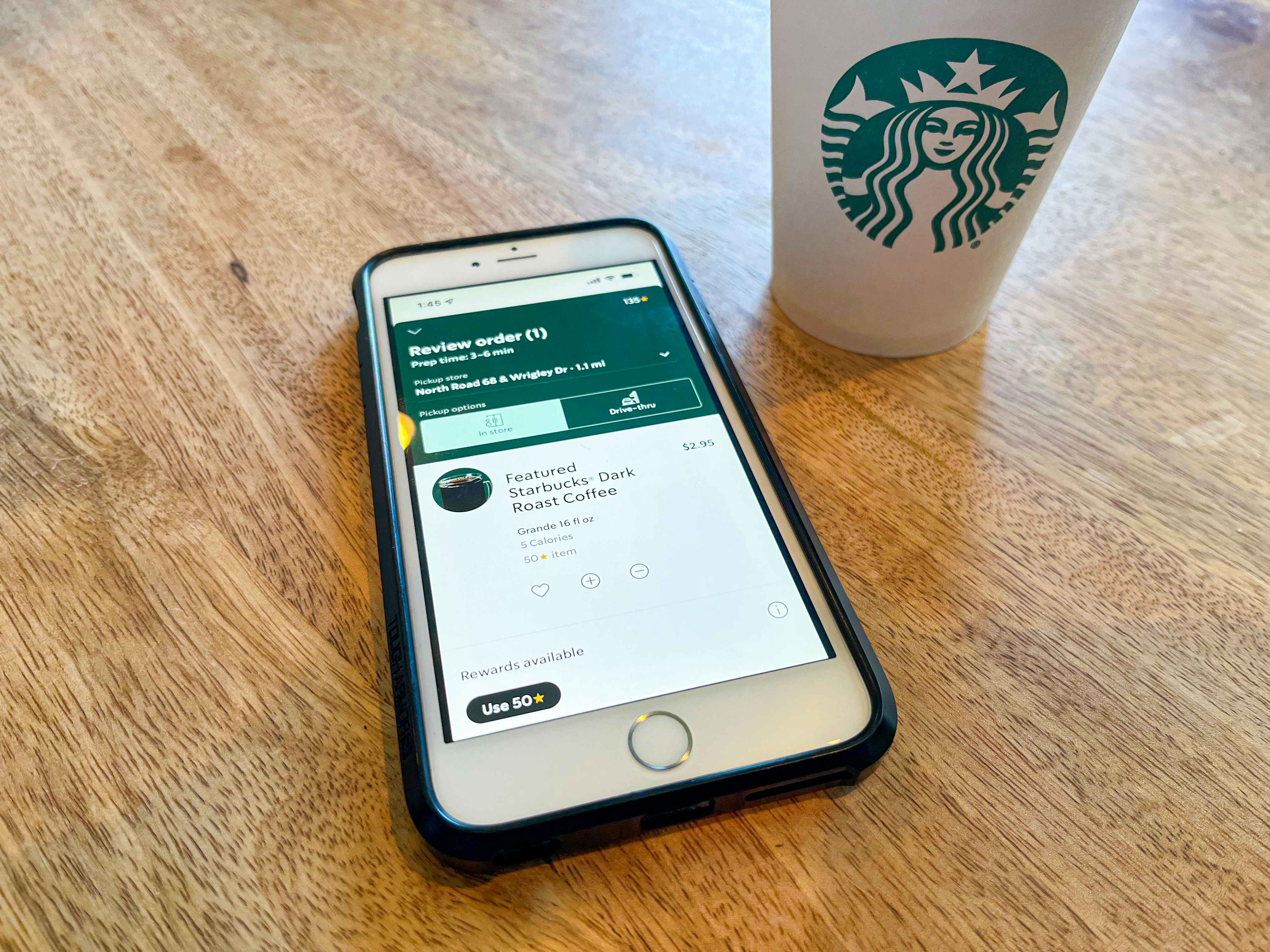 An iPhone on a table next to a Starbucks cup, displaying an order for a Grande Dark Roast Coffee on the Starbucks app.