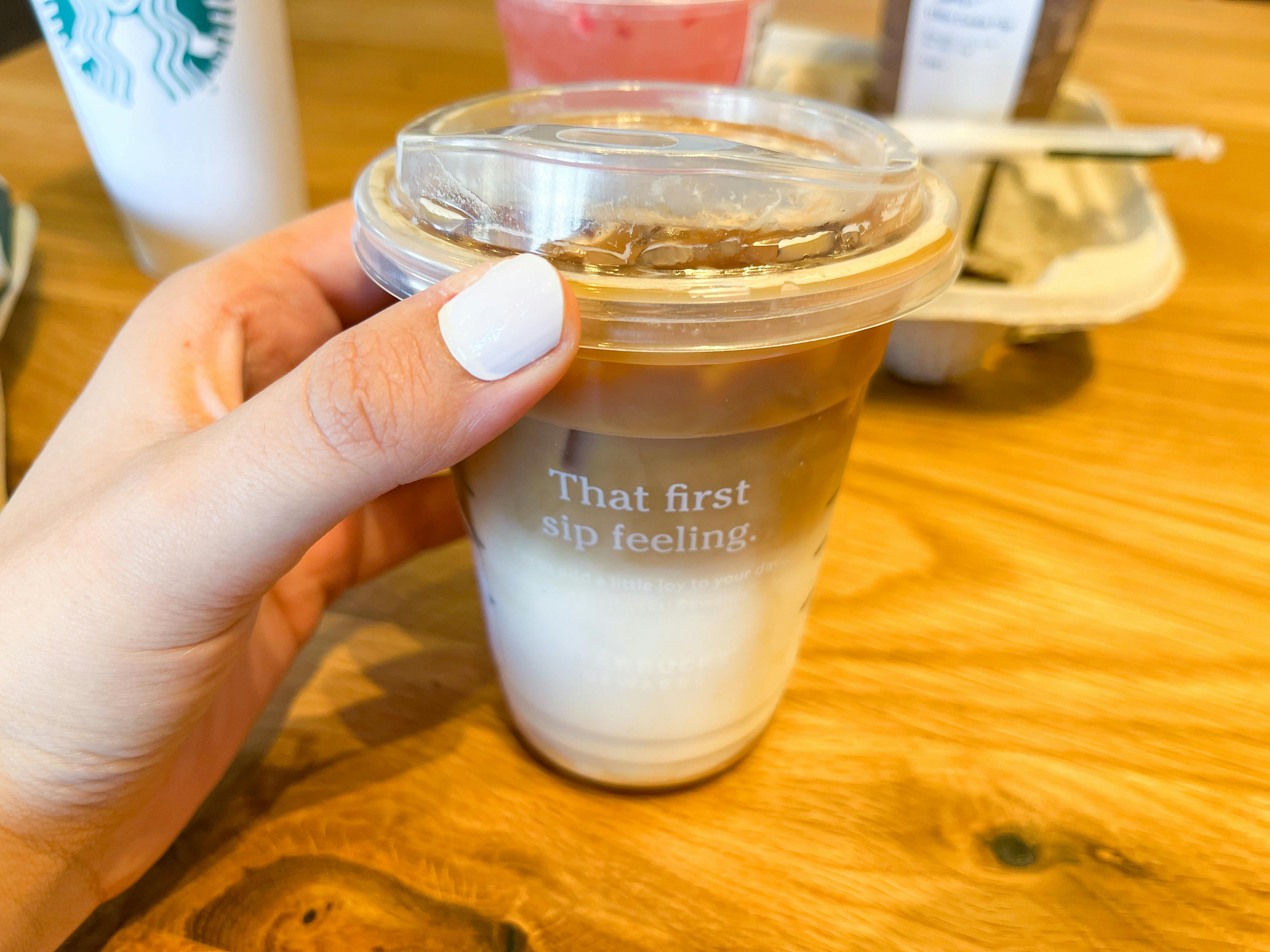 A person's hand picking up an iced Starbucks drink from a table inside Starbucks.