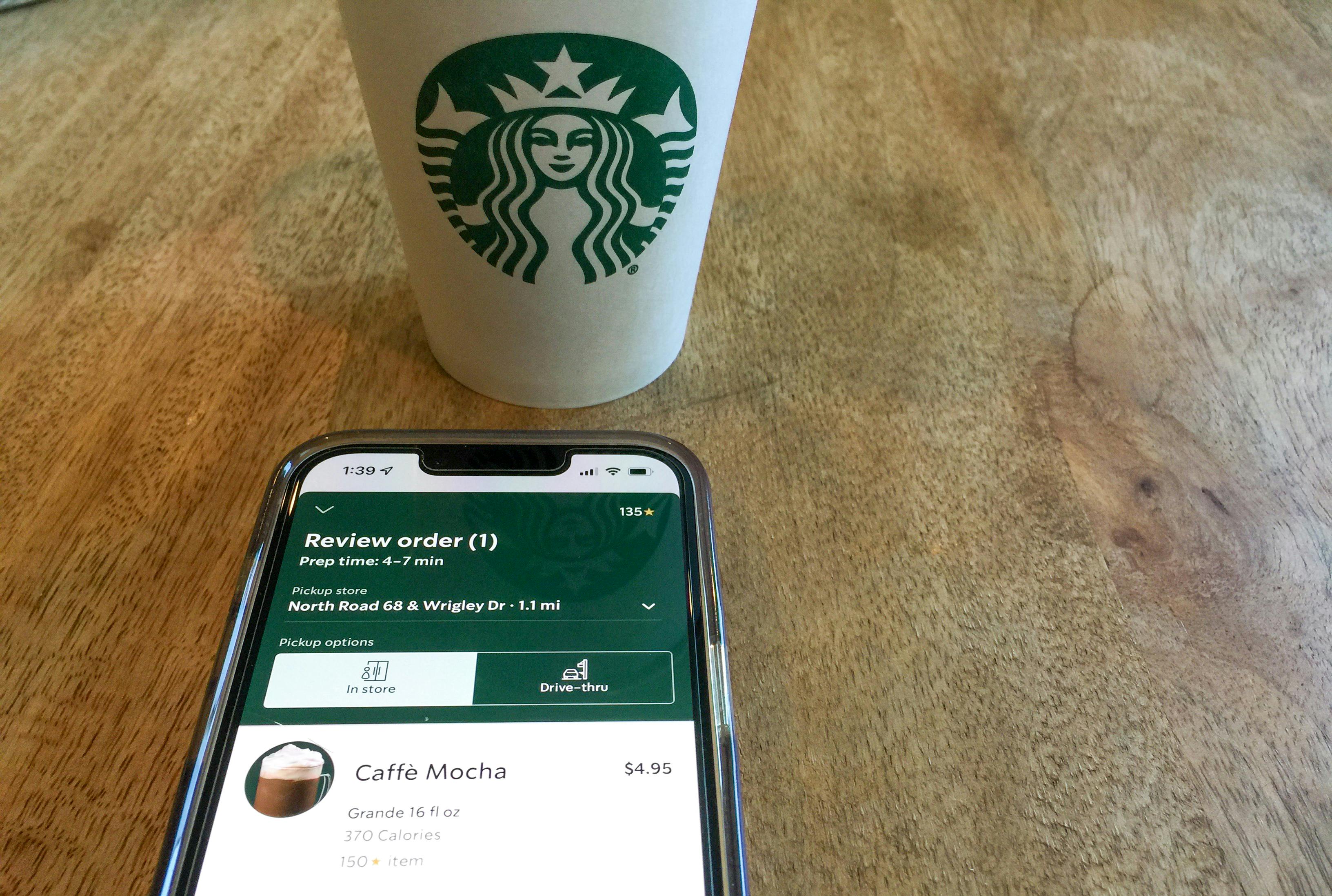 An iPhone on a table next to a Starbucks cup, displaying an order for a Grande Caffè Mocha on the Starbucks app.