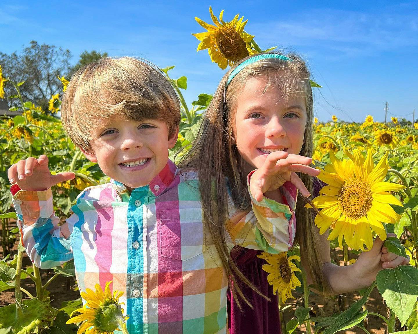 Two children standing next to each other and smiling while standing in a field of sunflowers.