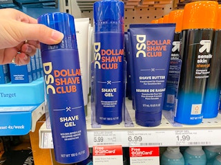 A person's hand holding up a bottle of Dollar Shave Club Shave Gel in front of a shelf with more Dollar Shave Products at Target.
