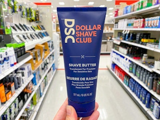 A person's hand holding up a bottle of Dollar Shave Club Shave Butter in an aisle at Target.