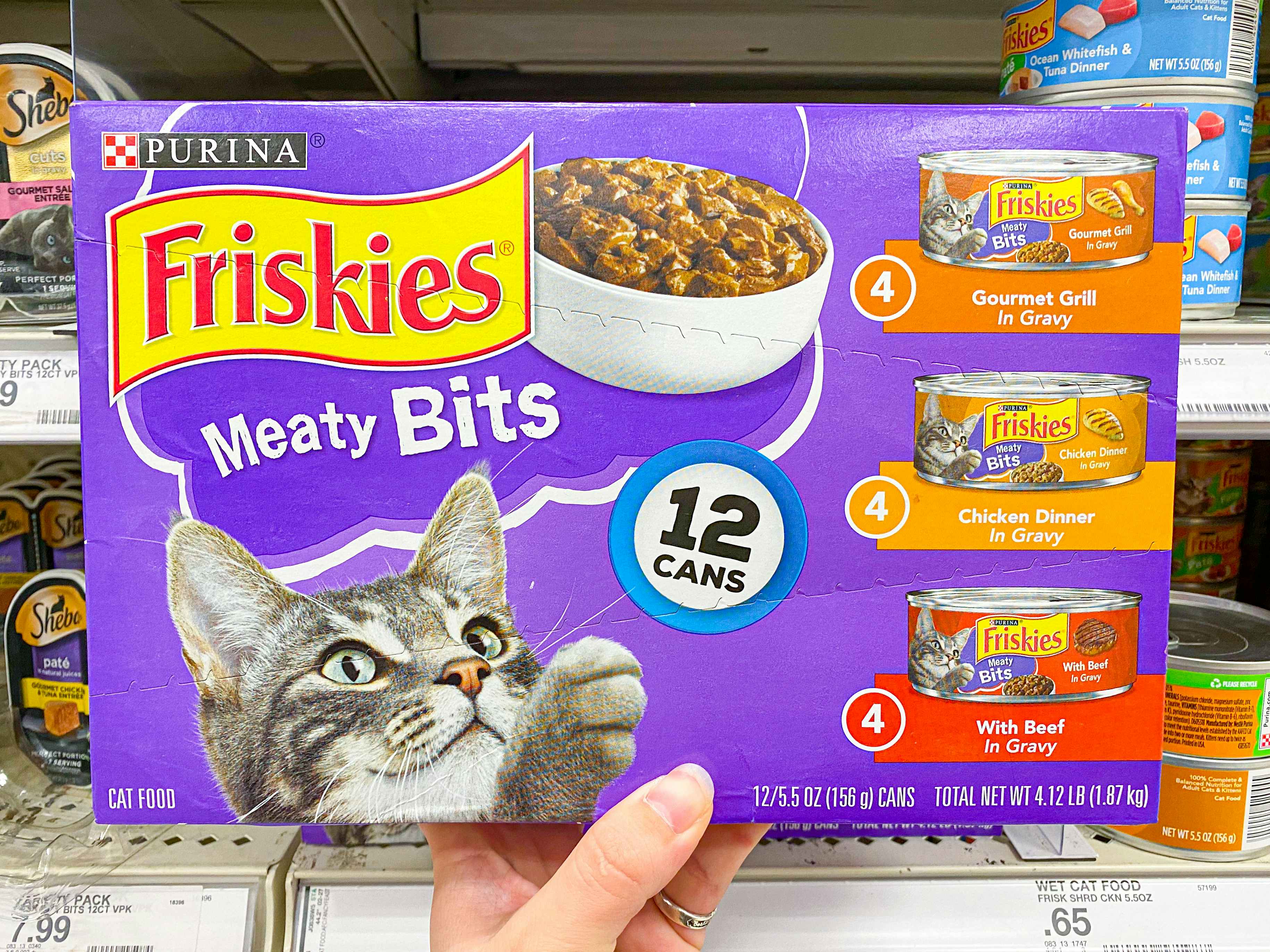 A person's hand holding up a box of Friskies Meaty Bits canned wet cat food in front of a shelf at Target.