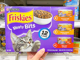 A person's hand holding up a box of Friskies Meaty Bits canned wet cat food in front of a shelf at Target.