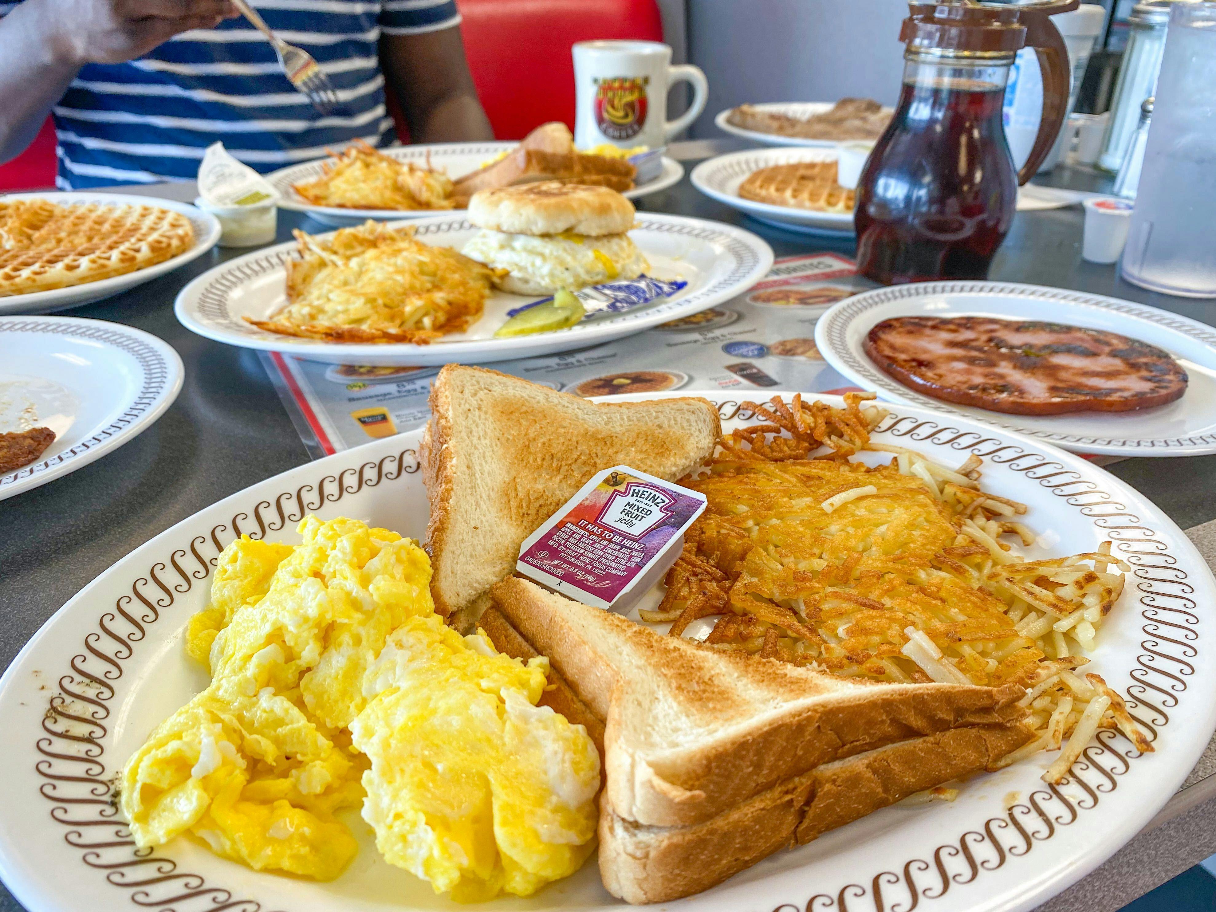 A table at Waffle House covered with plates of breakfast food, a syrup container, and drinks.