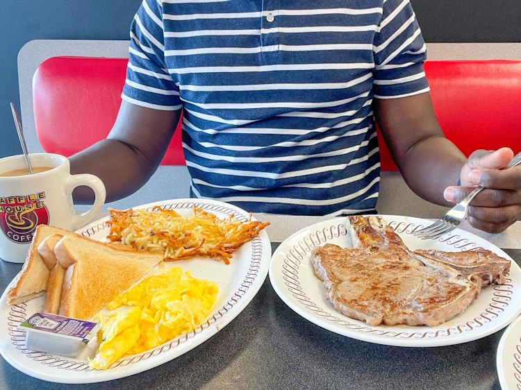 A person sitting in a booth at Waffle House with plates of food and a coffee mug sitting on the table in front of them.