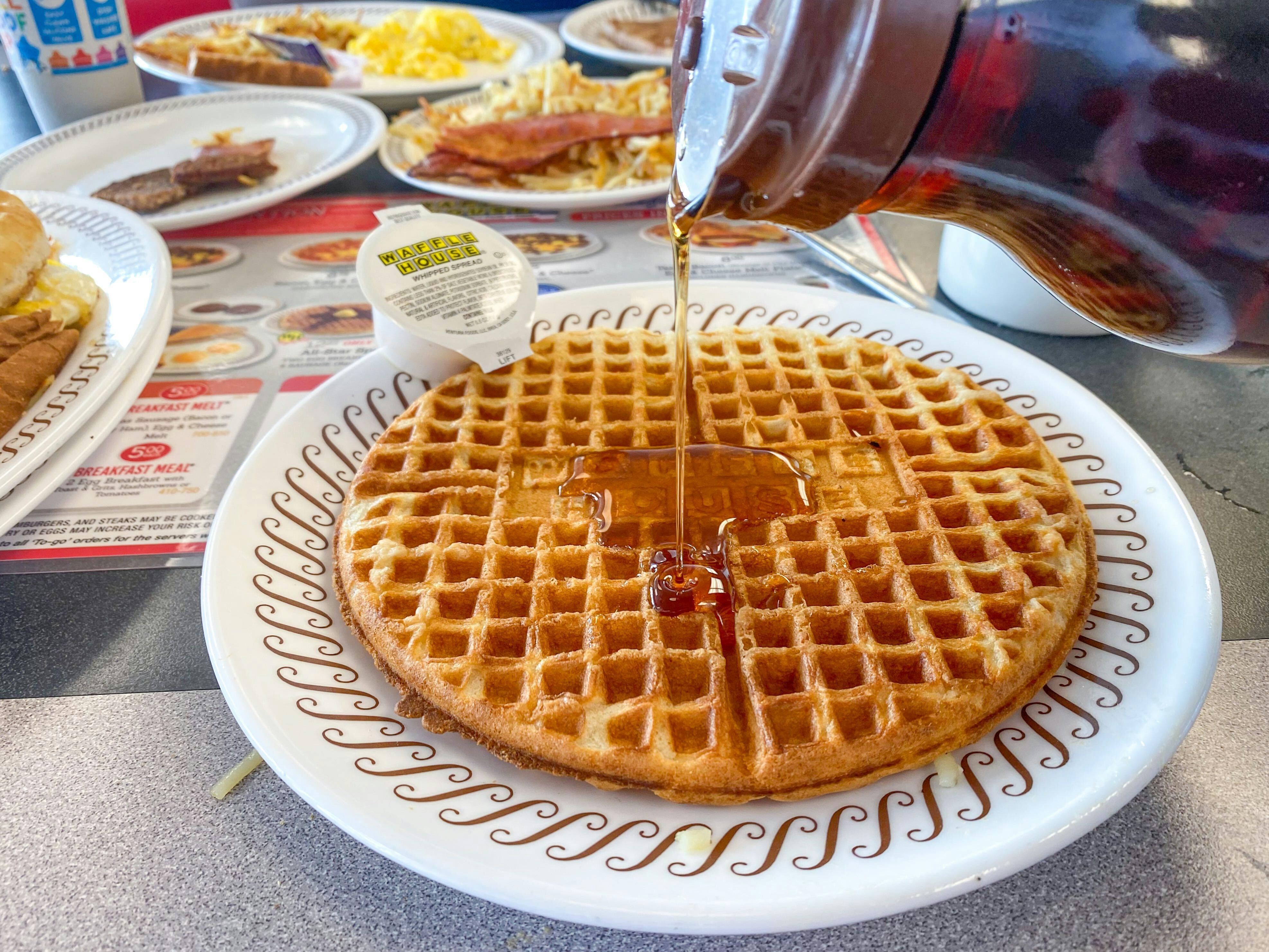 Someone pouring syrup onto a plated waffle on a table at Waffle House.