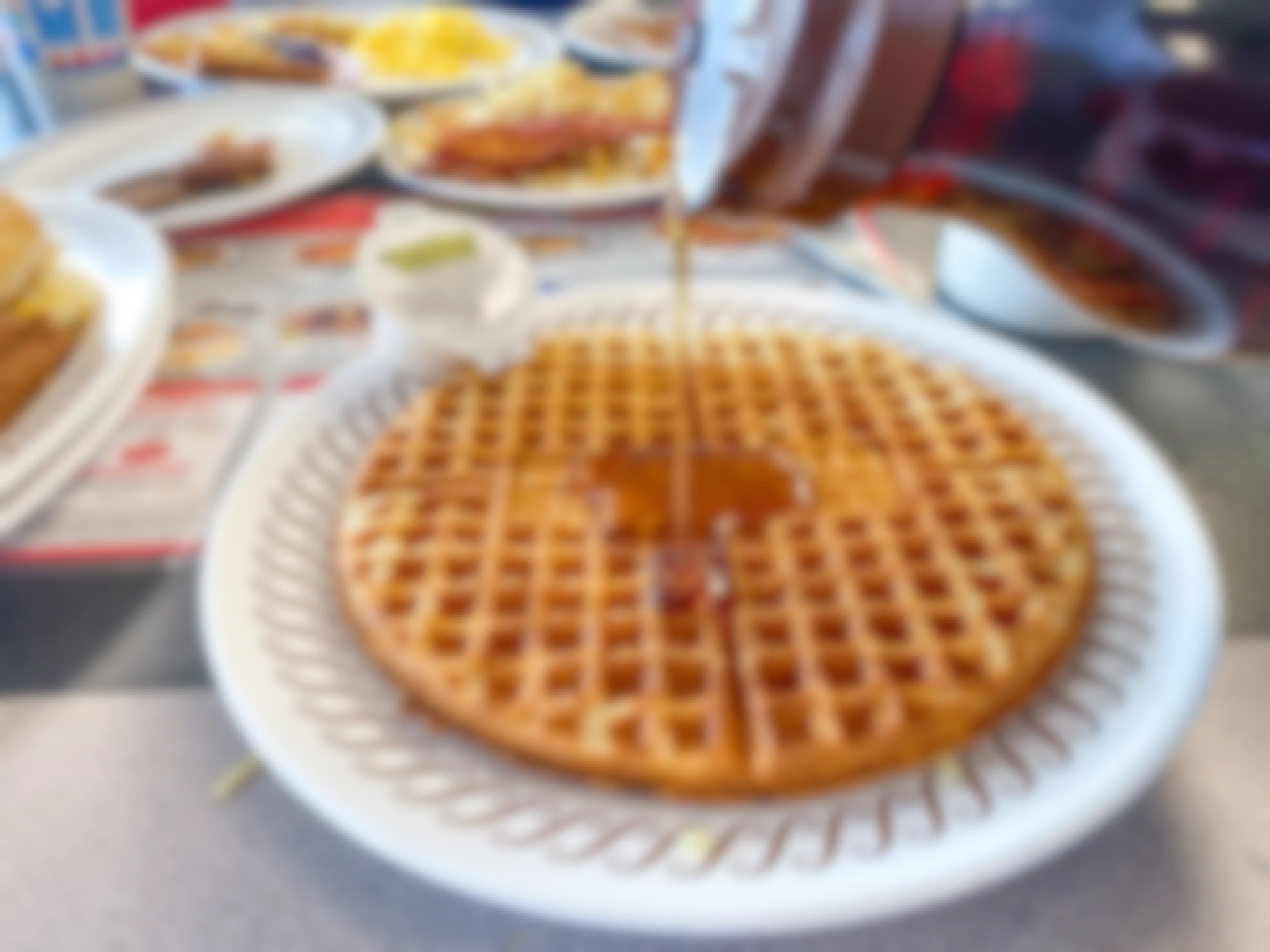 Someone pouring syrup onto a plated waffle on a table at Waffle House.