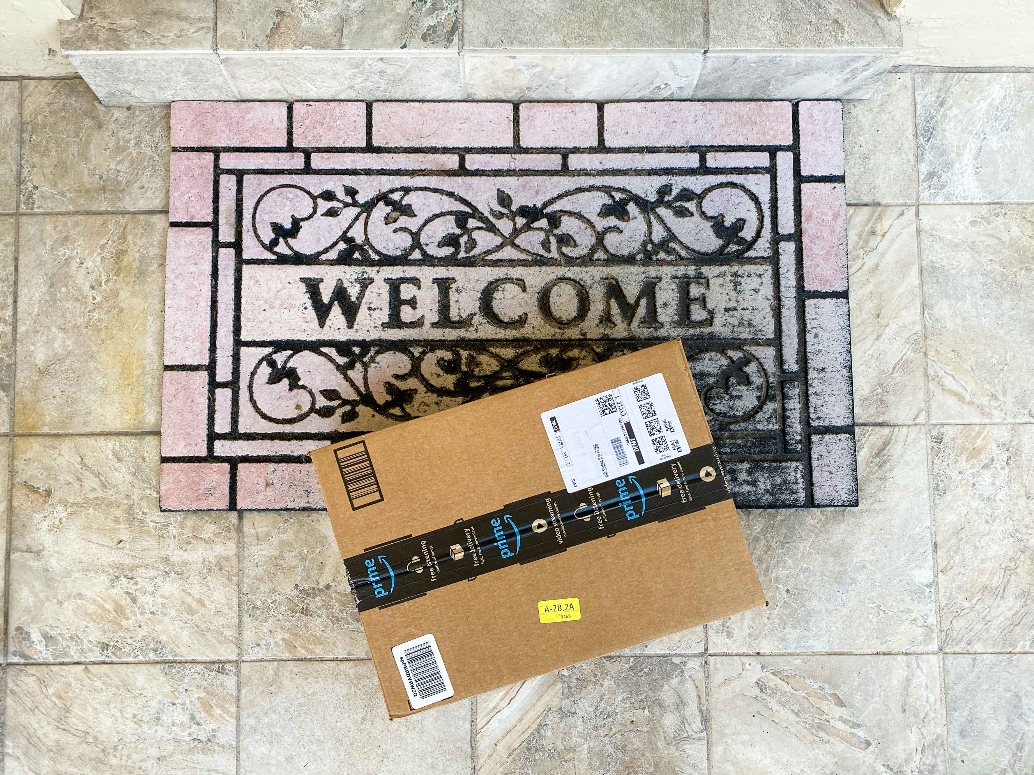 An Amazon box sitting on a welcome mat outside a front door.