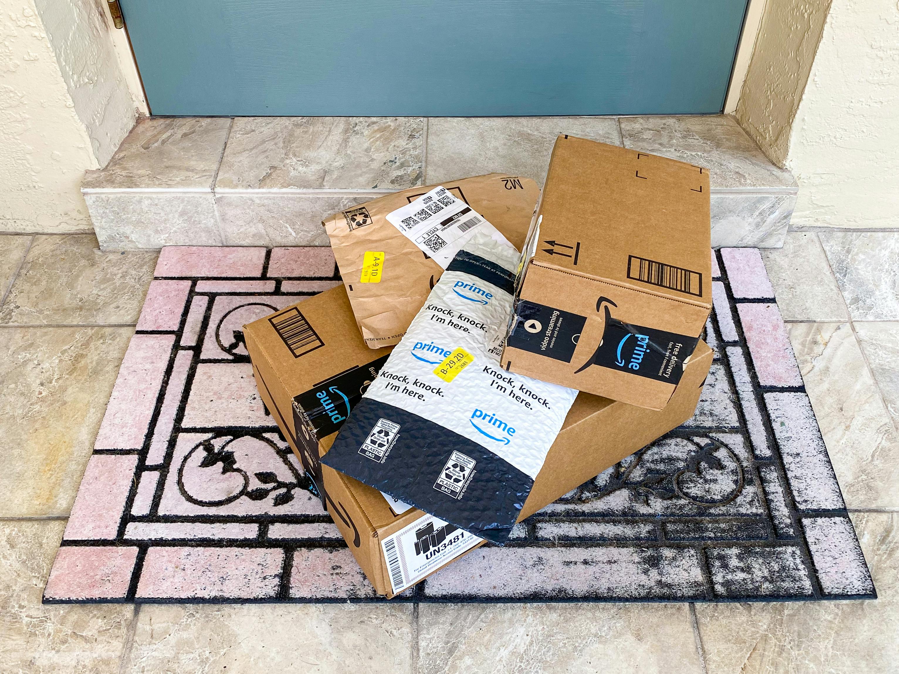 A pile of Amazon boxes and Amazon packing envelopes sitting on a doormat outside a front door.