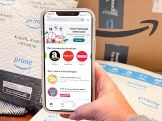 A cellphone displaying the ibotta app being held in front of Amazon boxes and packages