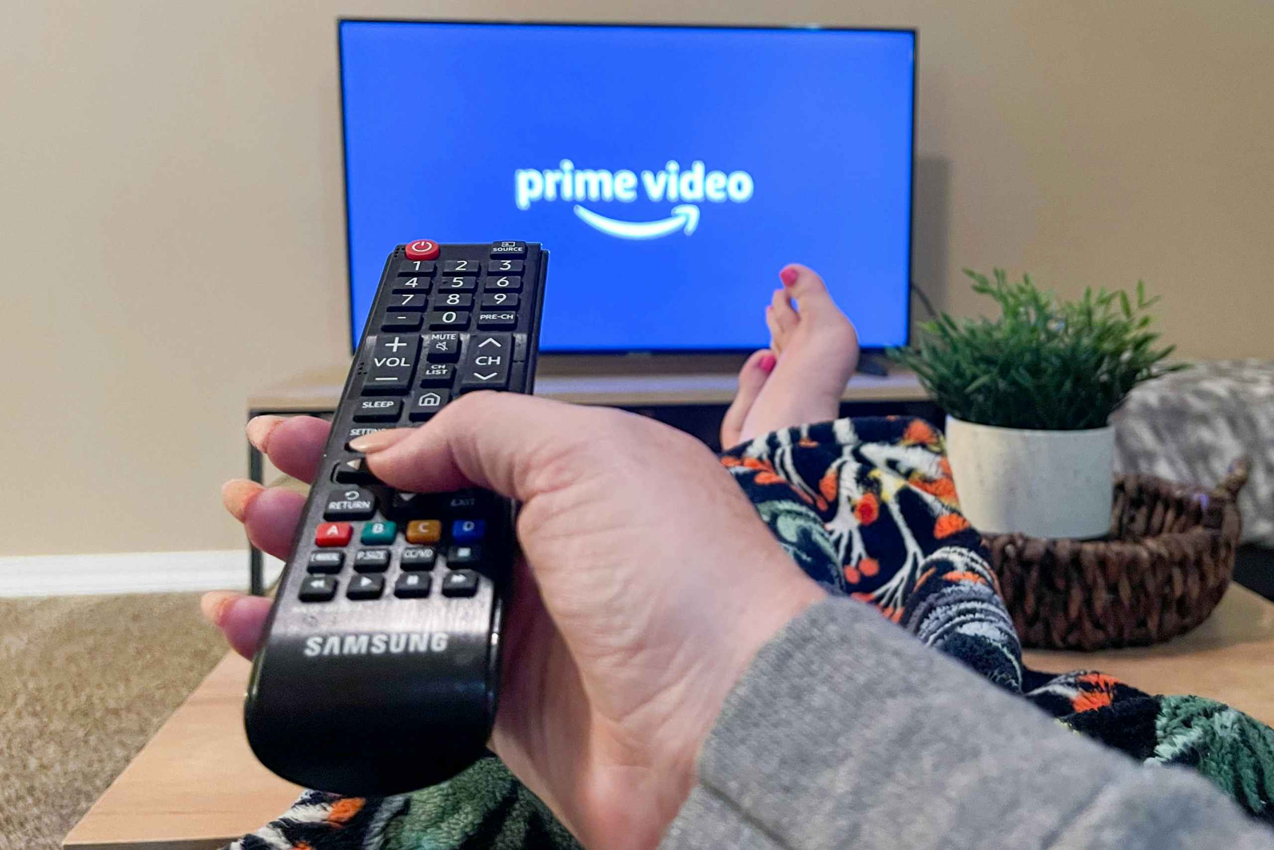 A person sitting on a couch with their feet up, pointing a remote at a TV with the Prime Video TV app's start-up screen displayed.