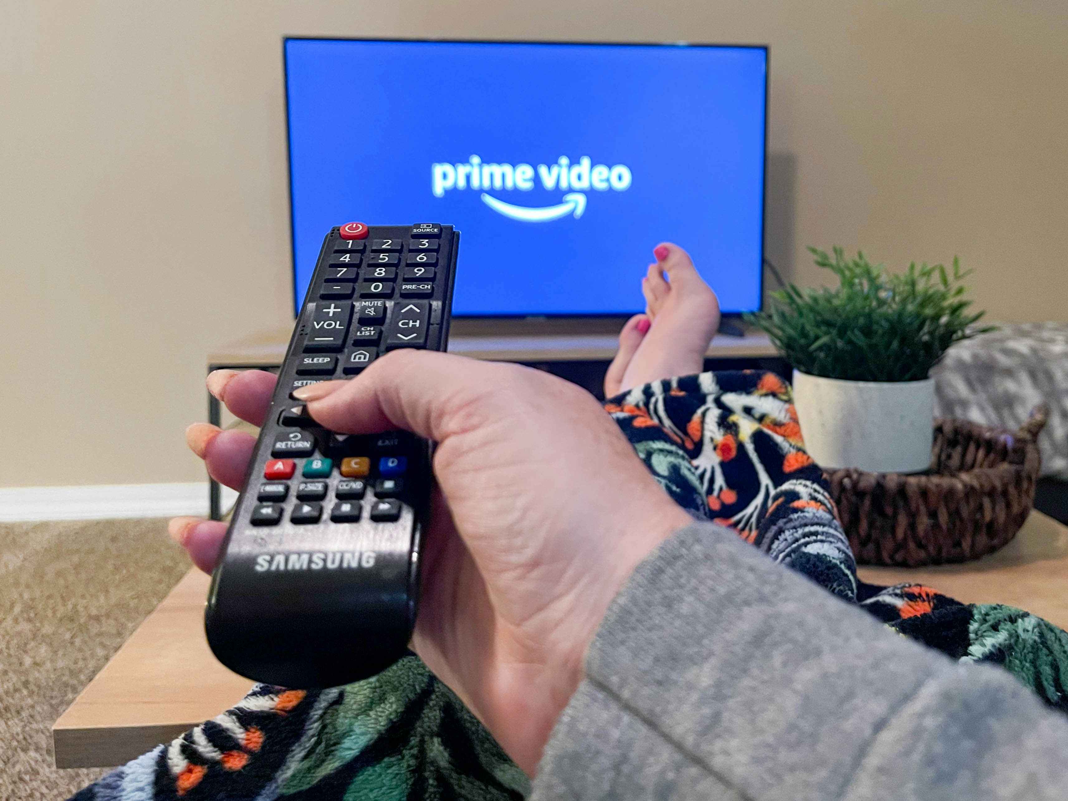 A person sitting on a couch with their feet up, pointing a remote at a TV with the Prime Video TV app's start-up screen displayed.